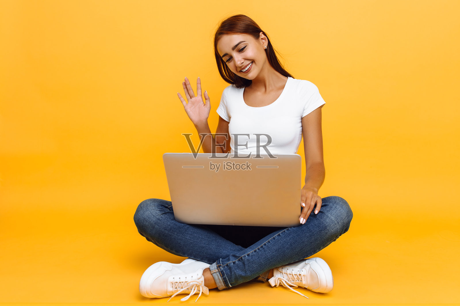 年轻漂亮的女孩拿着笔记本电脑，用黄色背景在Skype上聊天照片摄影图片