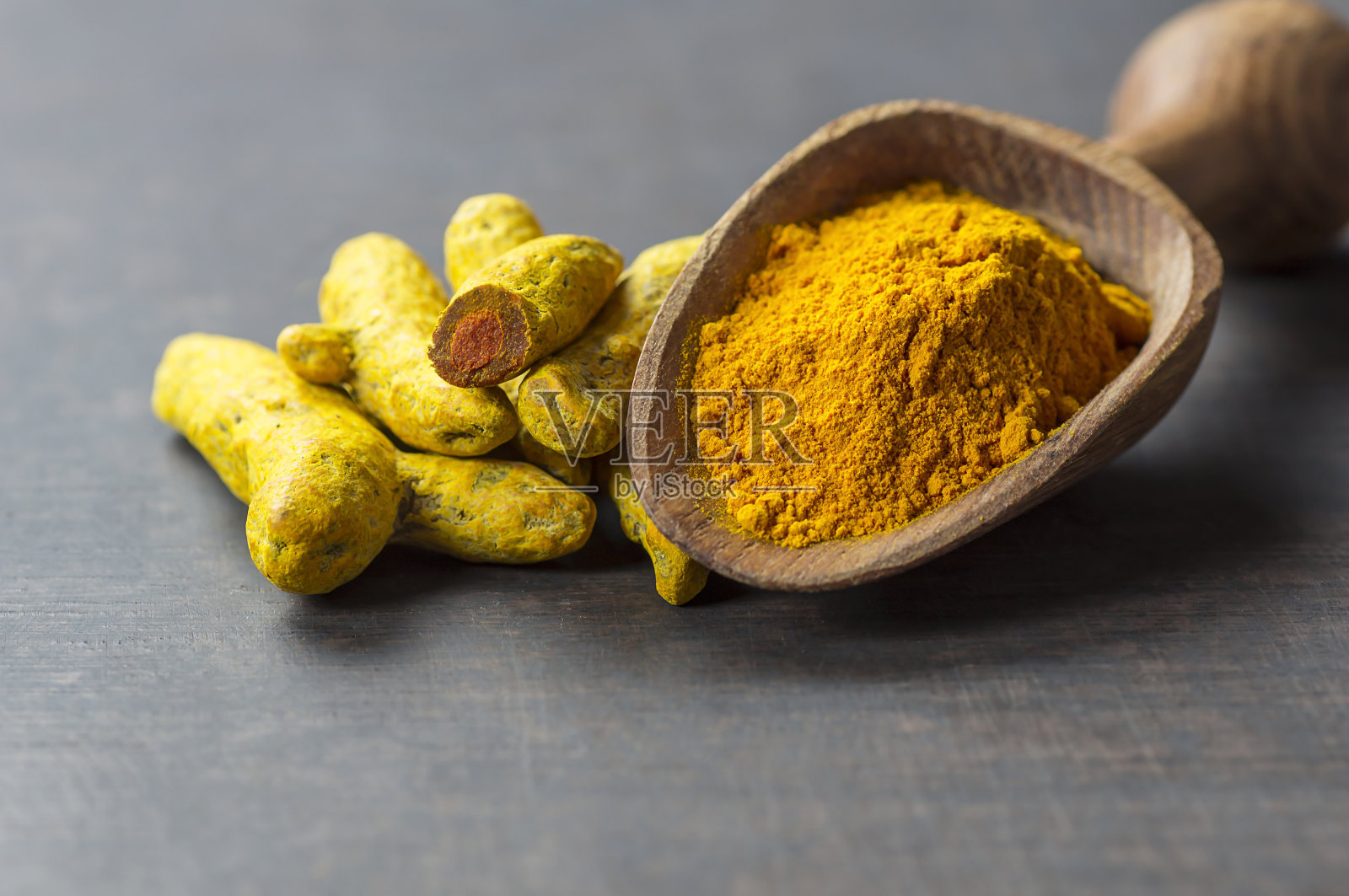 姜黄去皮根和姜黄粉在木勺或铲子在木制乡村背景，健康香料姜黄素(curcuma longa)照片摄影图片