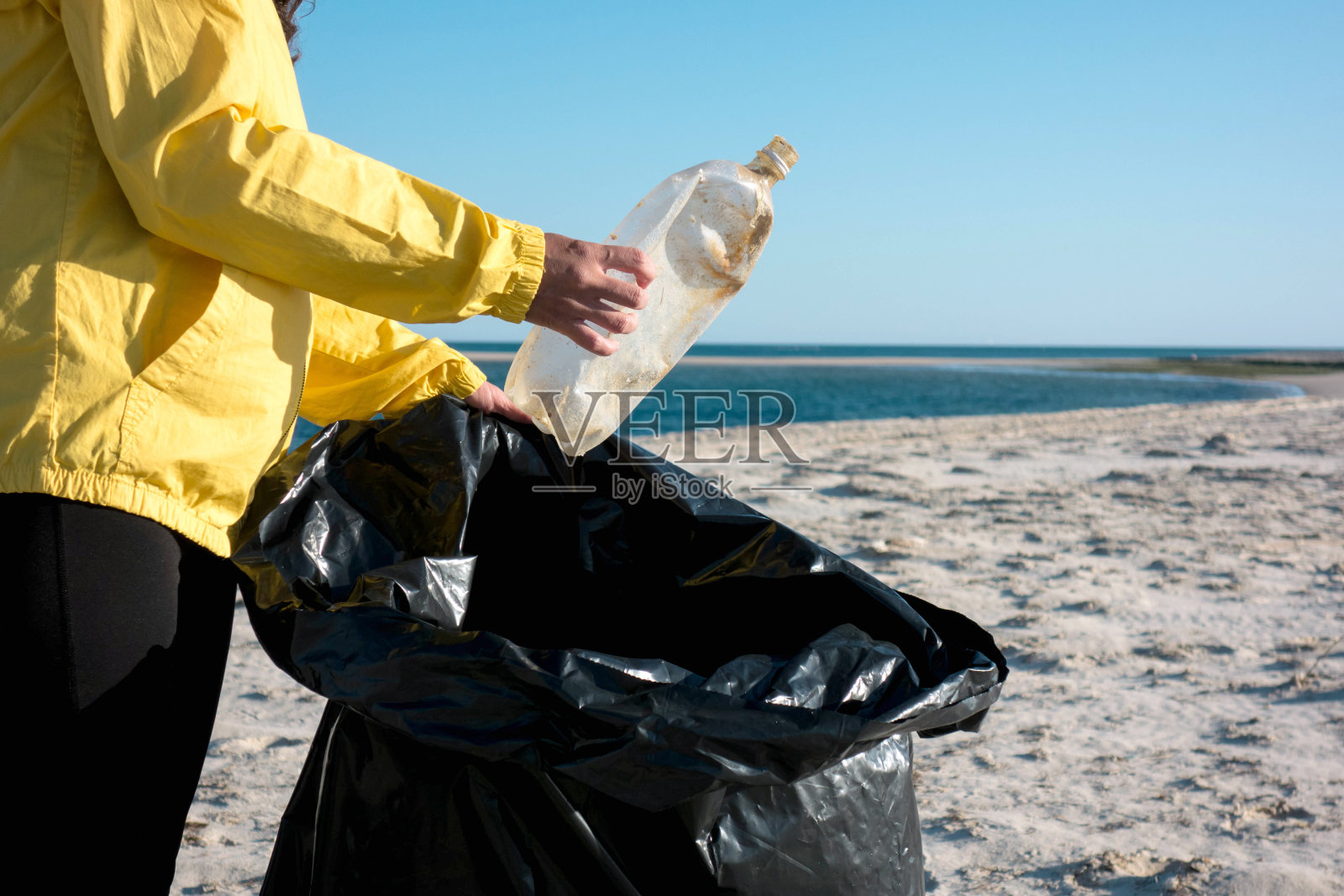 捡垃圾和塑料的女人用垃圾袋清理海滩。照片摄影图片
