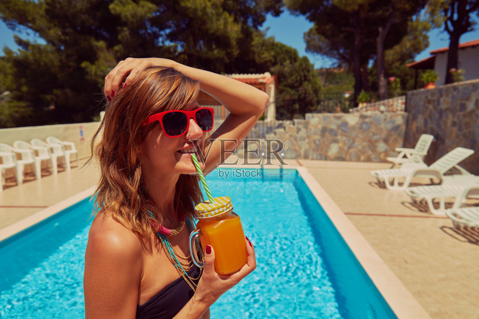 可爱的女人在游泳池里喝果汁。夏天的概念。照片摄影图片