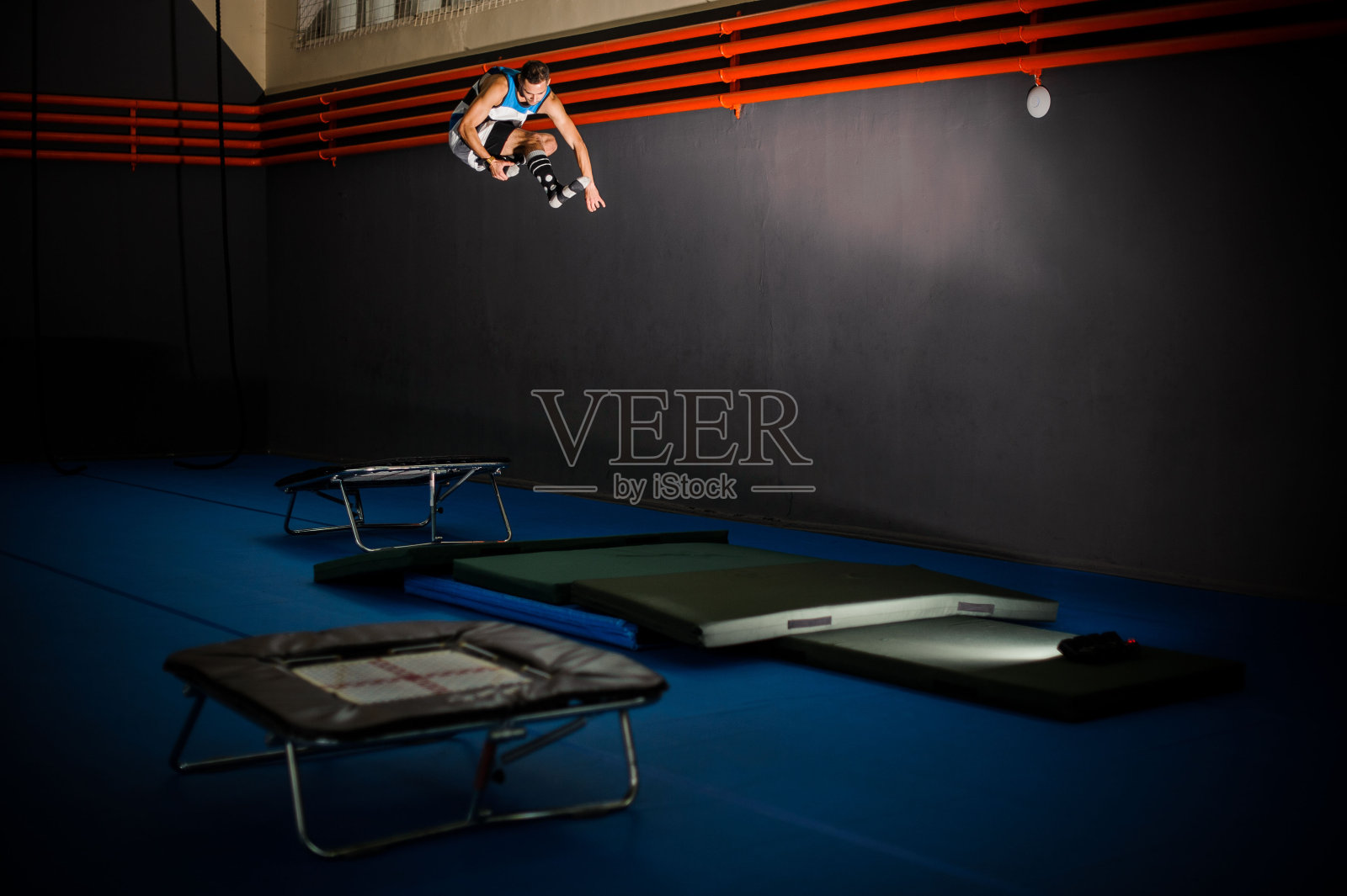 一个年轻人从小蹦床跳到体育馆的垫子上照片摄影图片