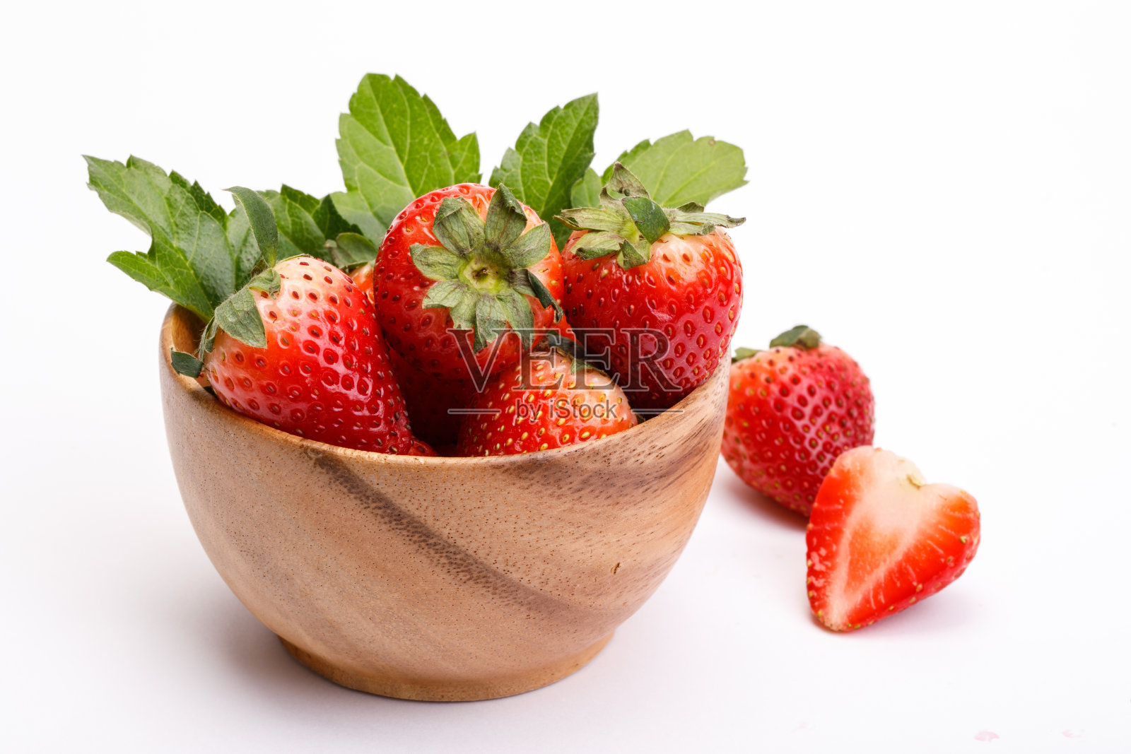红莓草莓在一个木碗孤立在白色的背景。木碗里装着带叶子的草莓。孤立的照片摄影图片