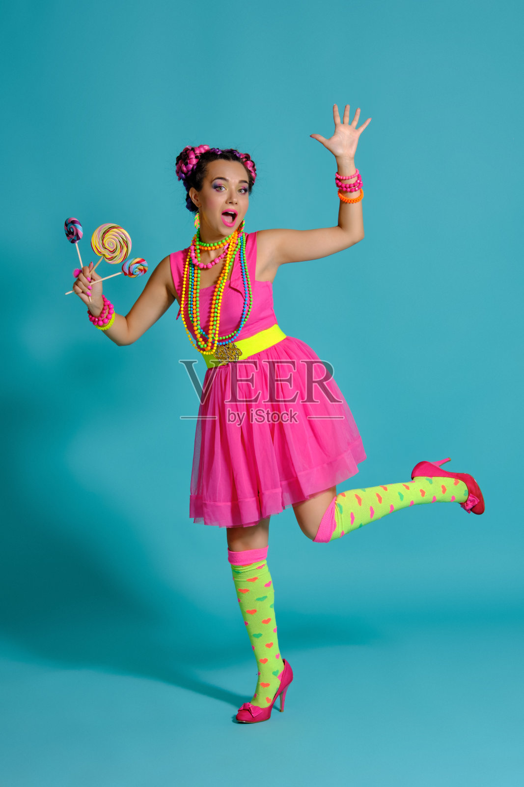 手持棒棒糖，在蓝色背景的影棚中摆姿势的可爱女孩照片摄影图片