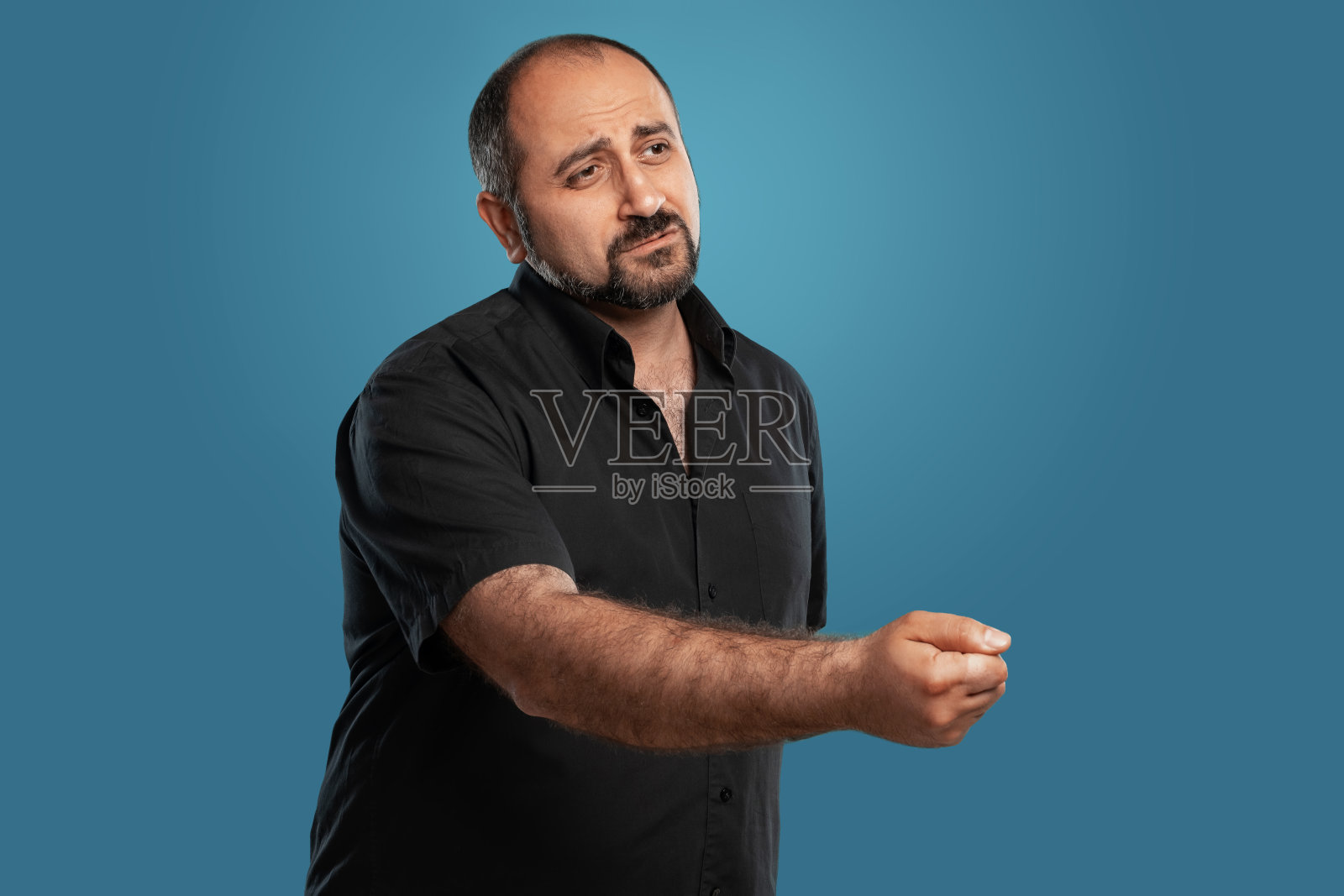 近距离的肖像一个黑发的中年男子的胡子，穿着黑色t恤和摆姿势的蓝色背景照片摄影图片