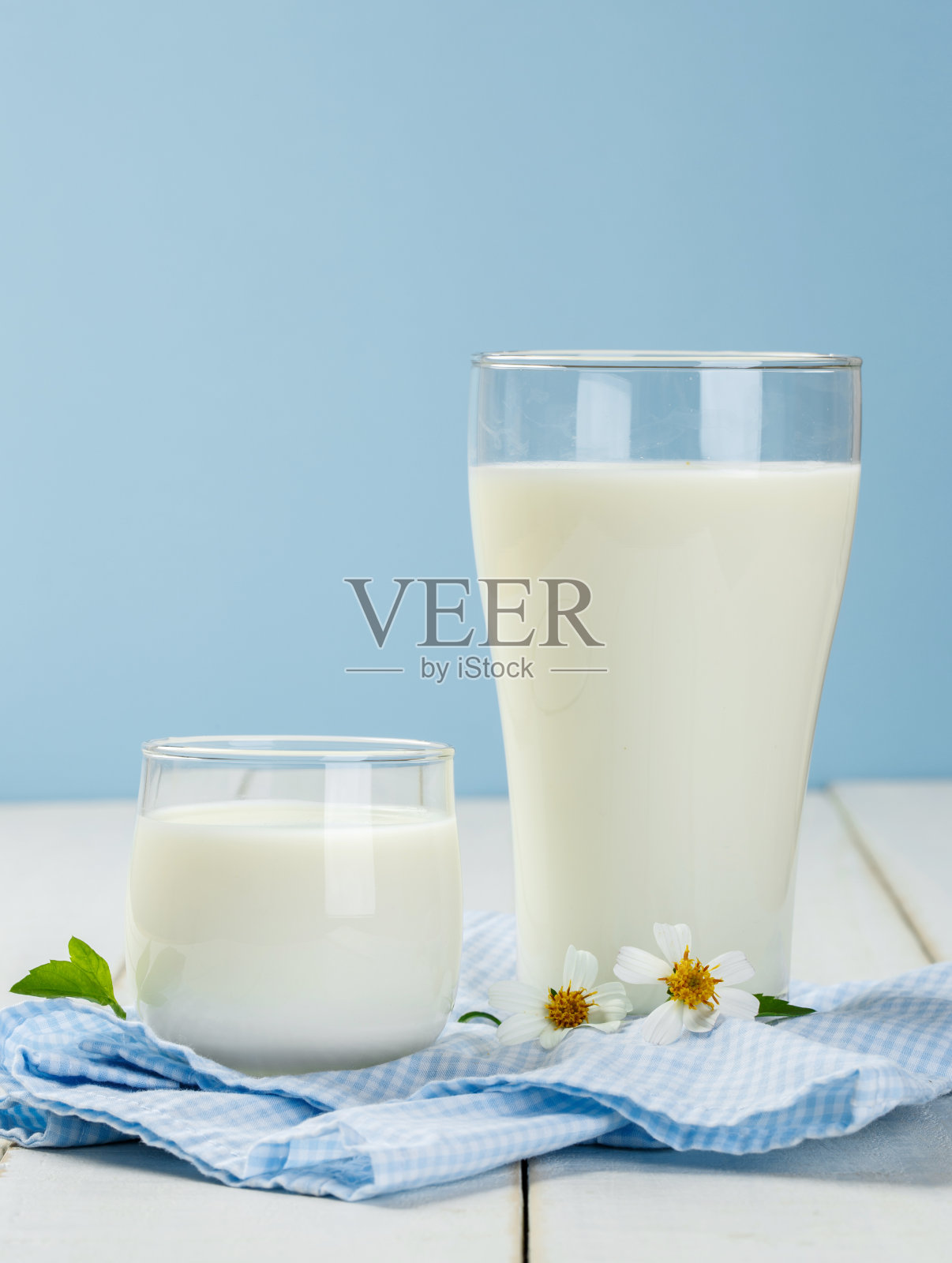 蓝色背景的白色木桌上放着一杯牛奶和餐巾照片摄影图片