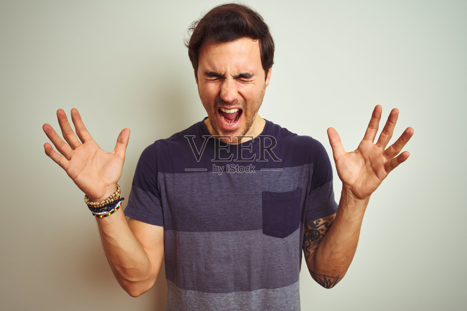 年轻英俊的纹身男子穿着休闲t恤，孤立的白色背景庆祝疯狂和疯狂的成功，举起手臂，闭上眼睛兴奋地尖叫。赢家的概念照片摄影图片