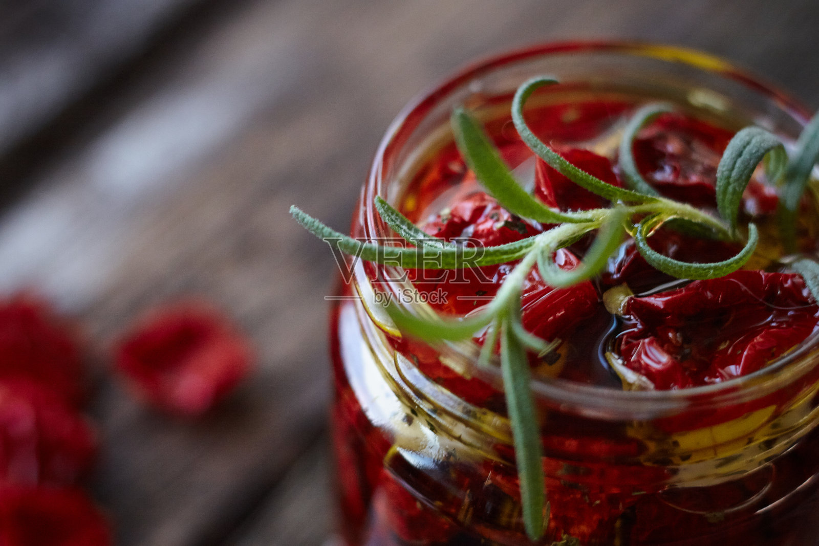 在一个质朴的木质表面上，用普罗旺斯香草、大蒜和橄榄油制作自制晒干番茄的罐子，选择性地聚焦照片摄影图片