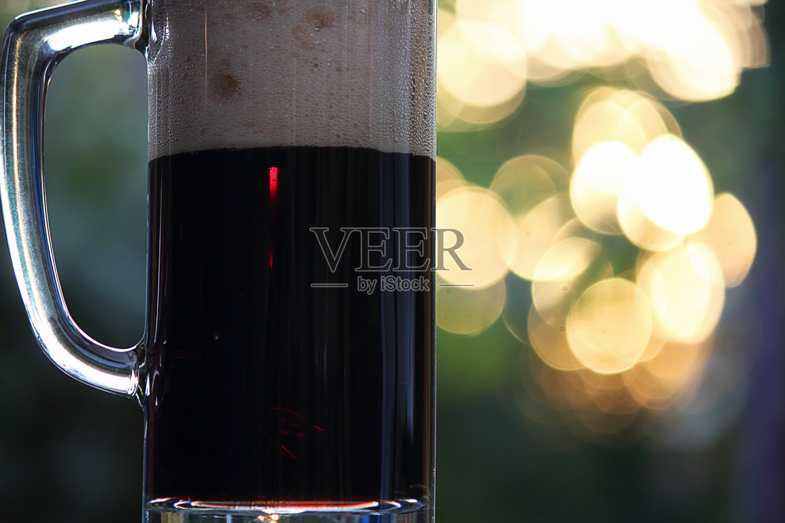 杯子里的啤酒。黑啤酒和泡沫。抽象的自然背景，日落。散景效果。照片摄影图片