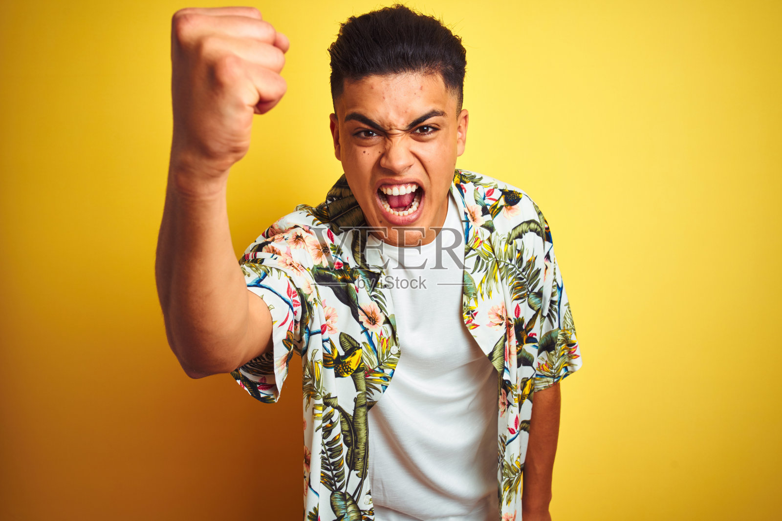 年轻的巴西人度假穿着夏天的花衬衫在孤立的黄色背景愤怒和疯狂举起拳头沮丧和愤怒，而大喊与愤怒。愤怒和侵略性的概念。照片摄影图片