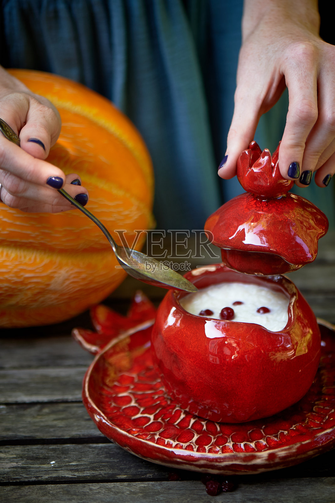 红色陶瓷,手工制作的。手榴弹形状的女人的手，打开锅盖盖上了粥。健康美味的早餐照片摄影图片