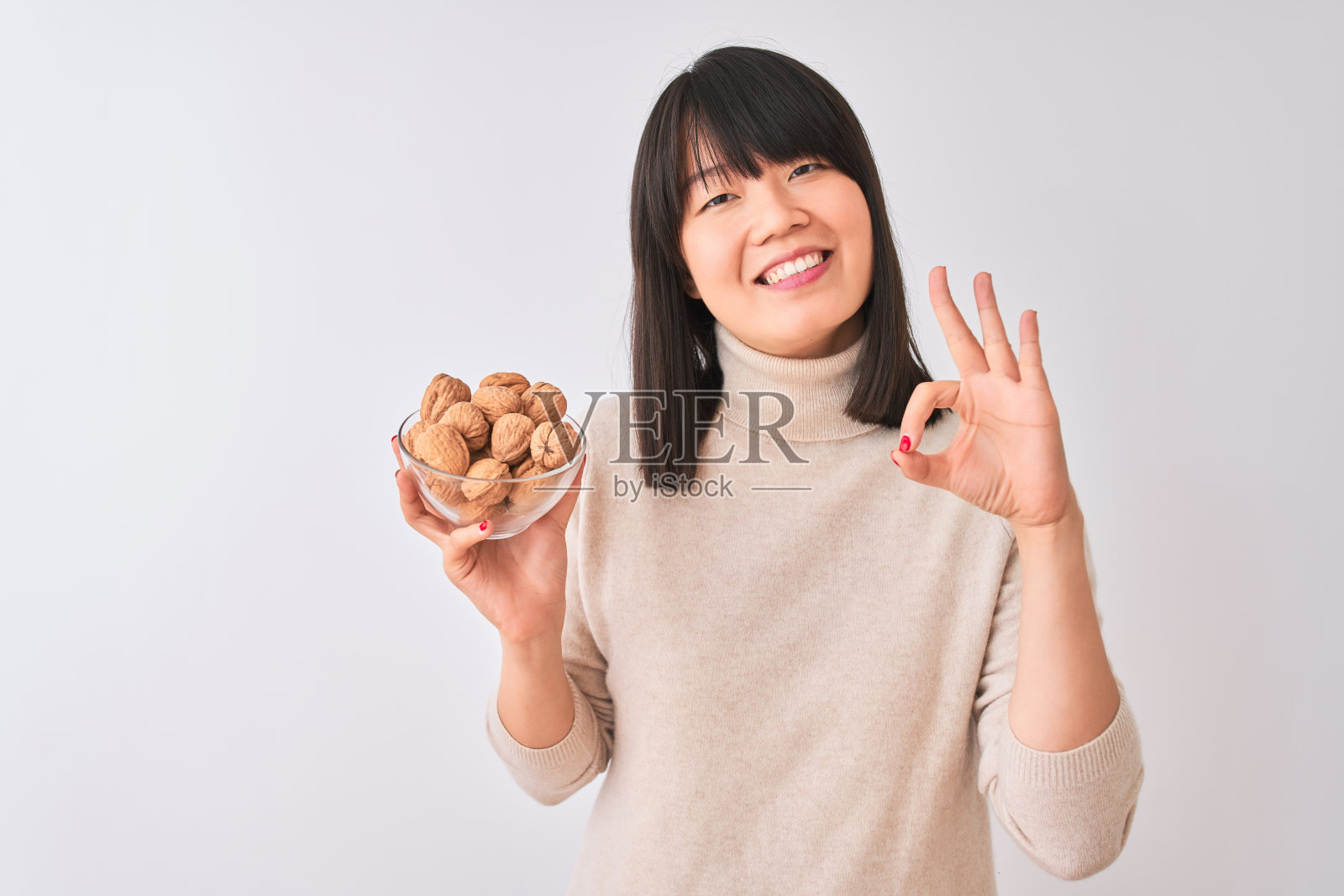 年轻美丽的中国女子拿着胡桃碗，在孤立的白色背景下用手指做ok手势，很好的象征照片摄影图片