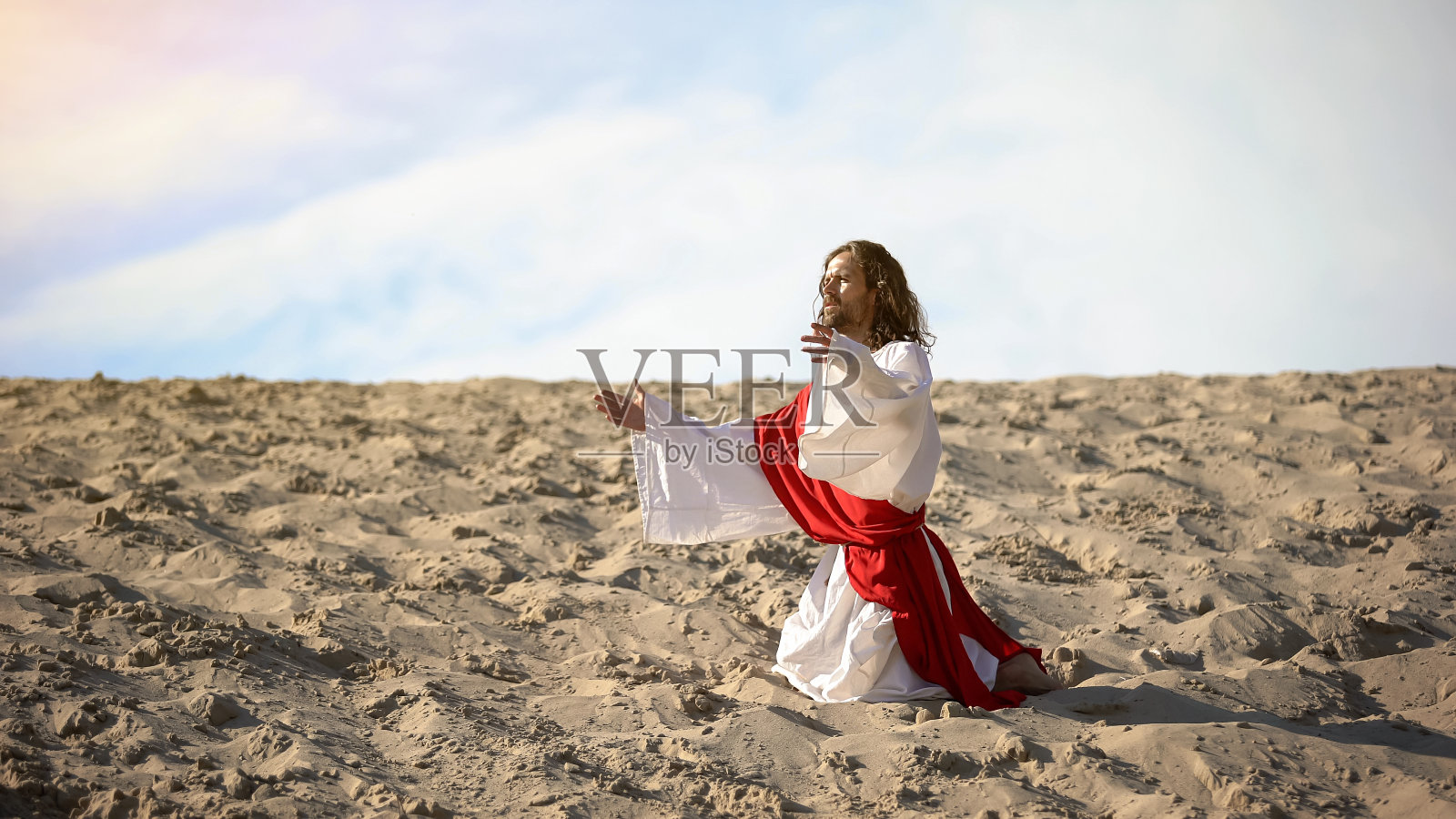 白袍男朝圣者跪在沙漠中，祈求天父的帮助，信仰照片摄影图片