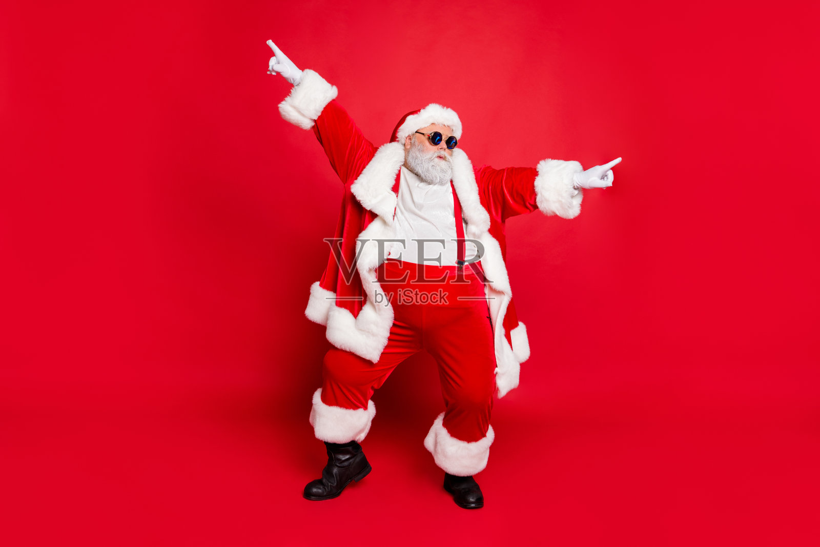 全身的funky胖圣诞老人与大滑稽的腹部跳舞举起手臂，戴着时尚时尚的眼镜孤立在红色的背景照片摄影图片
