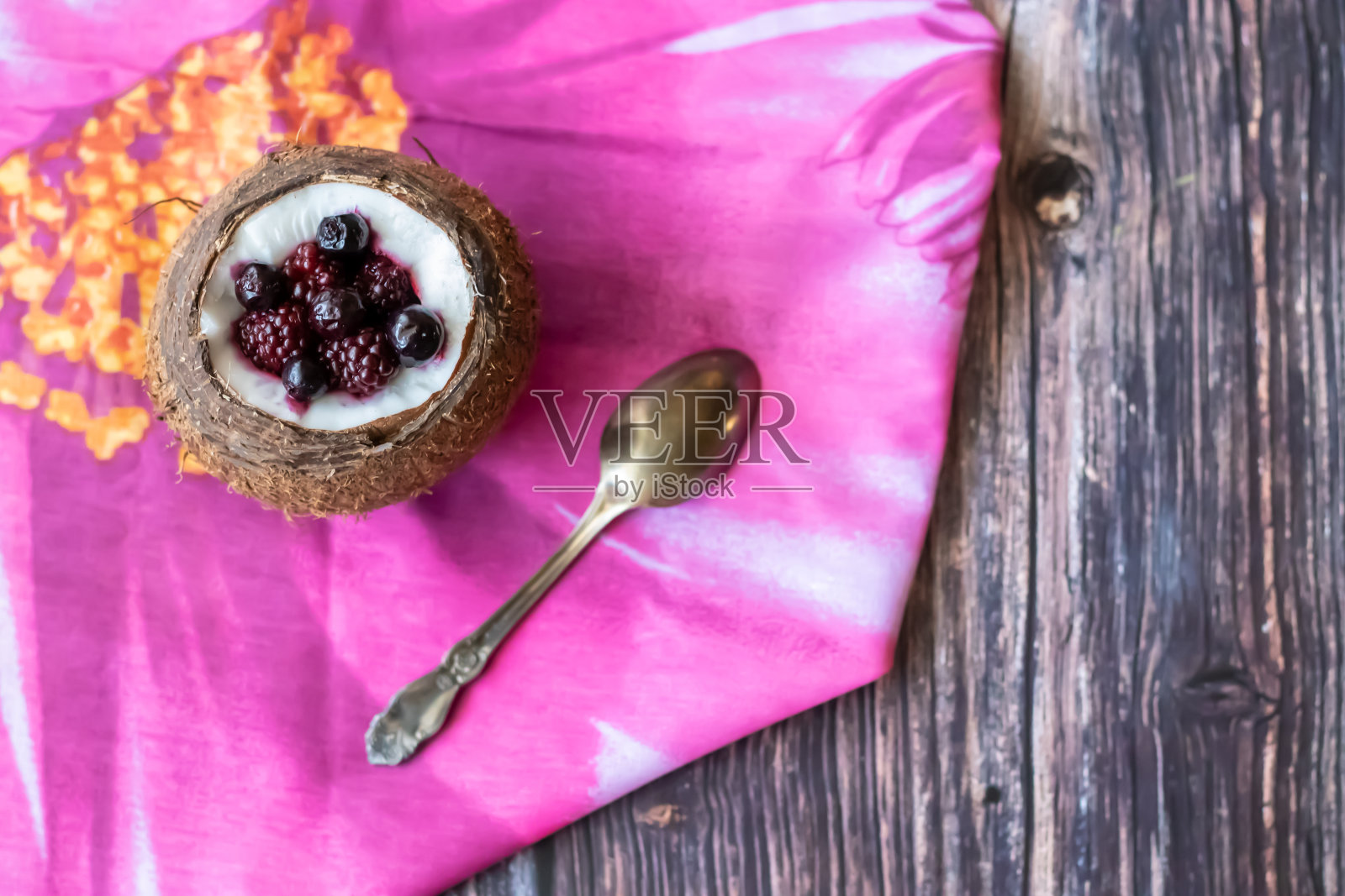 莓果甜点和酸奶在一杯椰子在木制的背景。黑莓，覆盆子，蓝莓，黑加仑子。粉红色的餐巾照片摄影图片