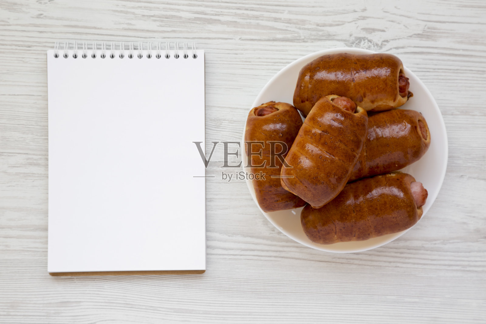 自制的牛肉香肠kolache放在白色的盘子里，白纸放在白色的木质背景上，俯视图。副本的空间。照片摄影图片