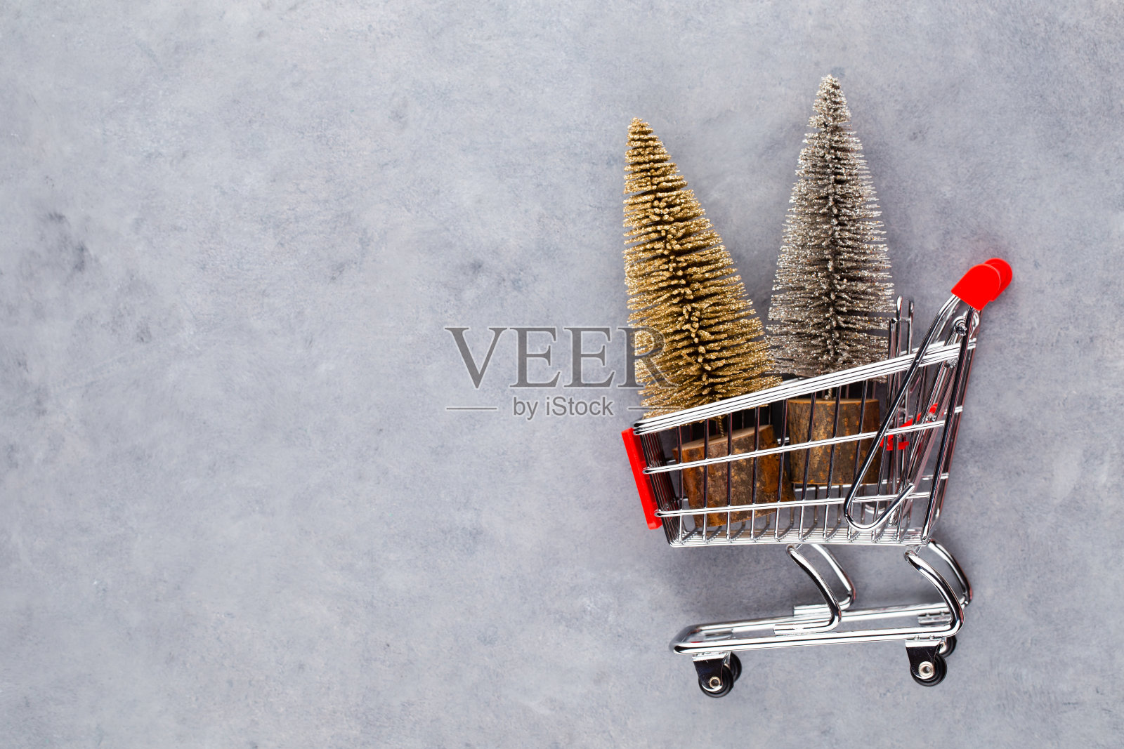 红色桌子上放着圣诞树的购物车。照片摄影图片