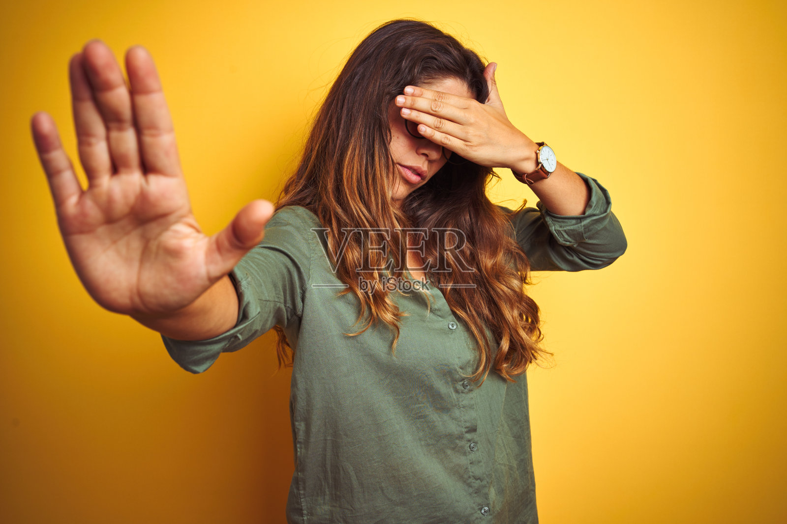 年轻美丽的女人穿着绿色的衬衫和眼镜在黄色孤立的背景覆盖眼睛的手和做停止手势与悲伤和恐惧的表情。尴尬和消极的概念。照片摄影图片