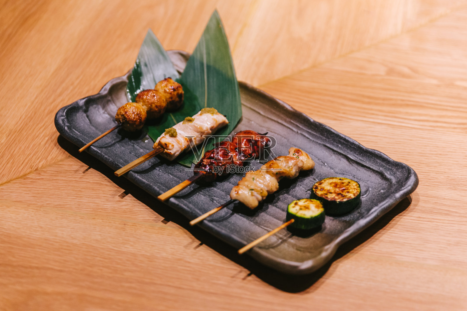 烤鸡肉串(日式烤鸡串)配以鸡肉、内脏和黄瓜，盛于黑石盘上。照片摄影图片