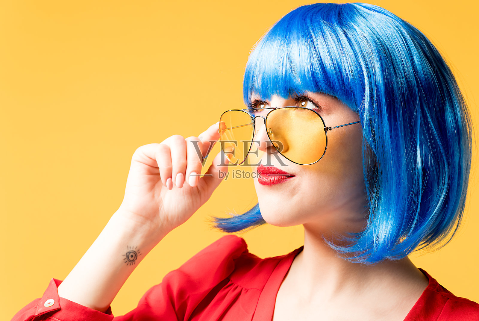 漂亮的年轻女子，戴着蓝色假发，黄色背景上戴着黄色太阳镜照片摄影图片