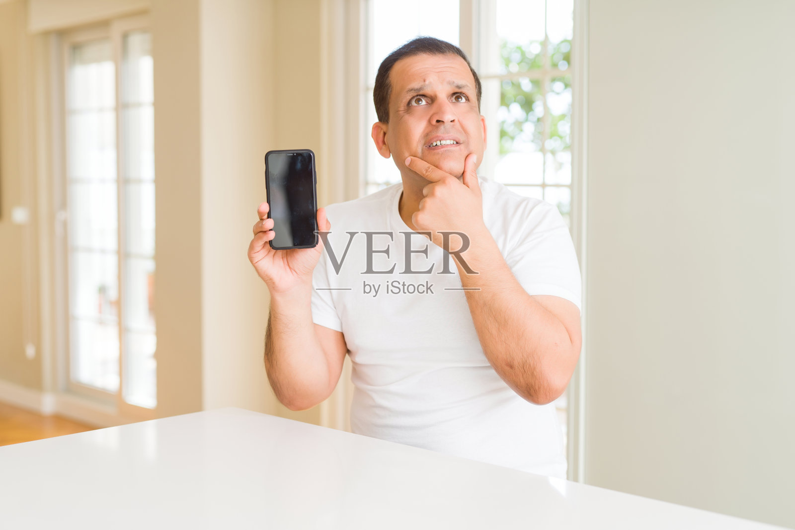 中年男子看着智能手机屏幕严肃地面对思考问题，非常困惑的想法照片摄影图片