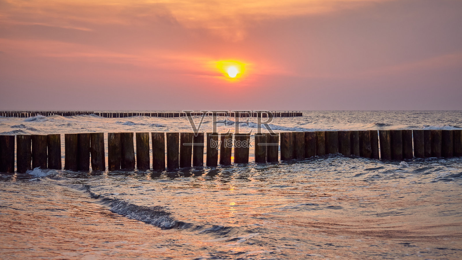日落时从海滩上看到的木制防波堤。照片摄影图片