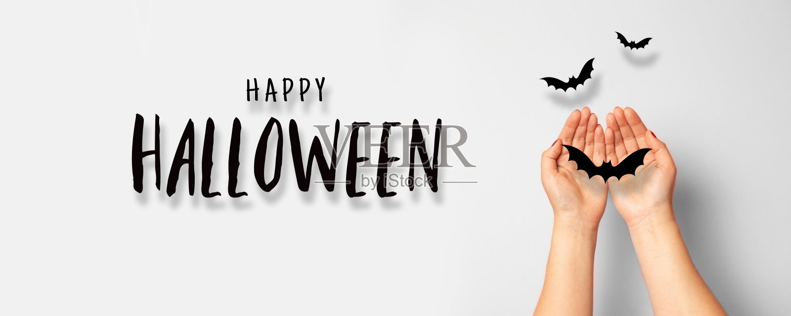 万圣节的概念。灰色背景上的女性手握黑色的纸蝙蝠。照片摄影图片