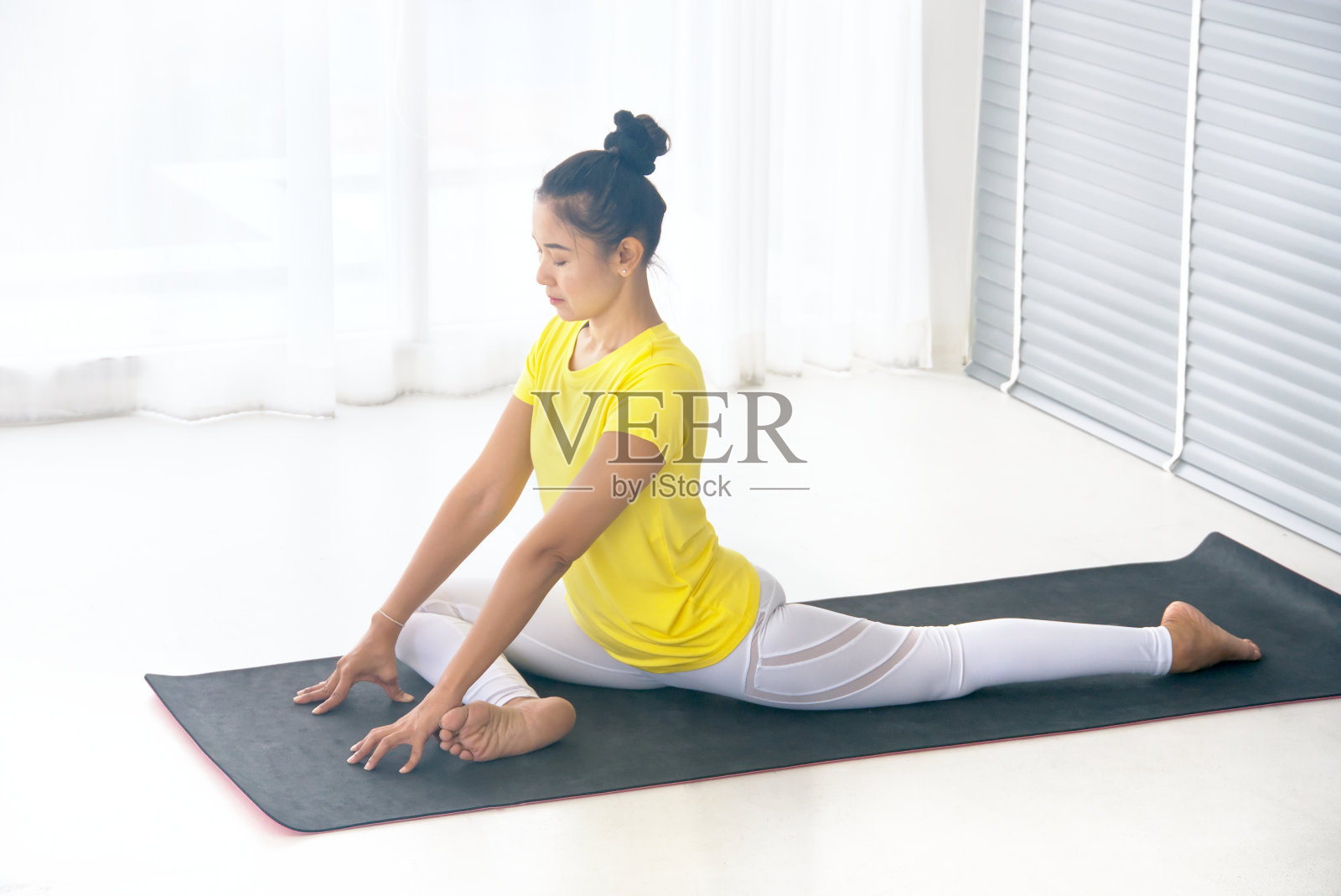 瘦弱的亚洲妇女穿着黄色运动t恤练习瑜伽练习“国王鸽子姿势”，在早上放松靠近窗户，健康的概念。照片摄影图片