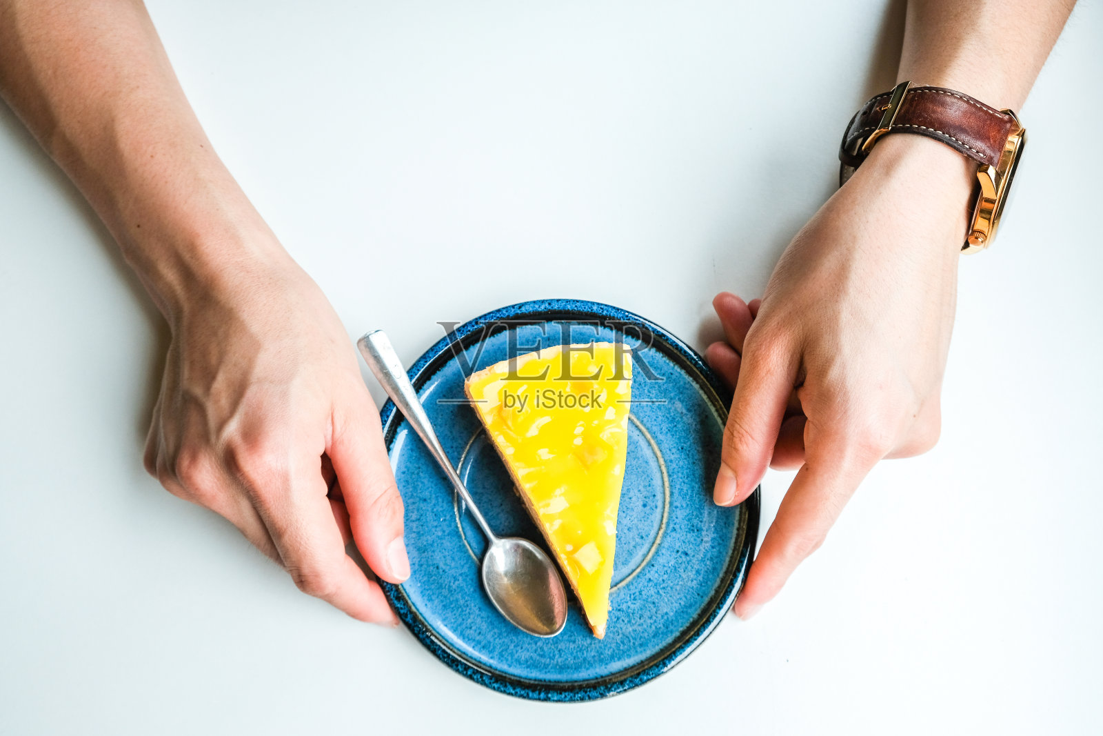 在孤立的白色桌子上，女人的手触摸着一个装有自制菠萝芝士蛋糕的盘子。照片摄影图片