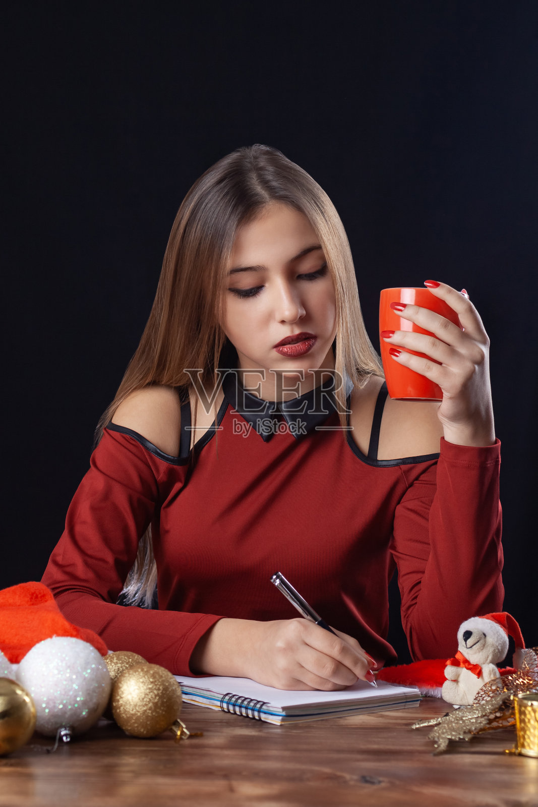 美丽的女孩喝热饮和写在黑色的背景在红色新年装。照片摄影图片