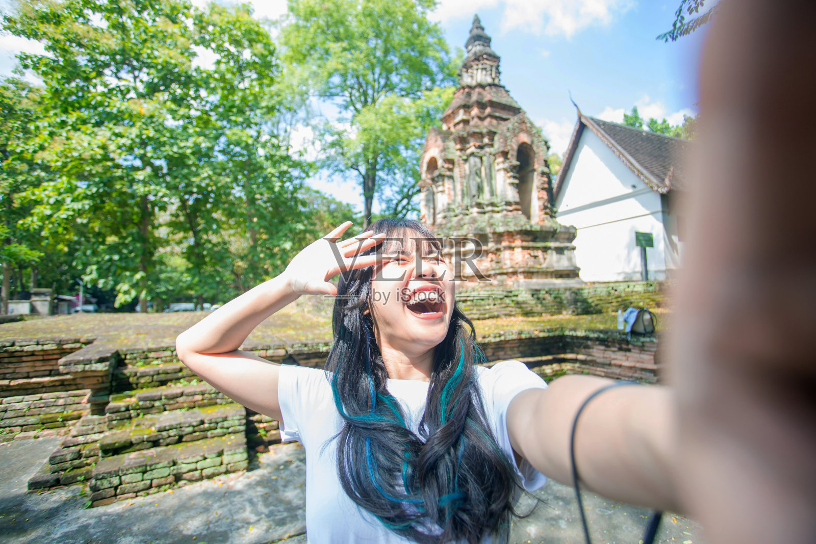 近距离拍摄美丽的亚洲女性步行到古老的寺庙，并通过网络媒体拍摄自己。她是一个美丽的微笑。玩得开心，牙齿干净。照片摄影图片