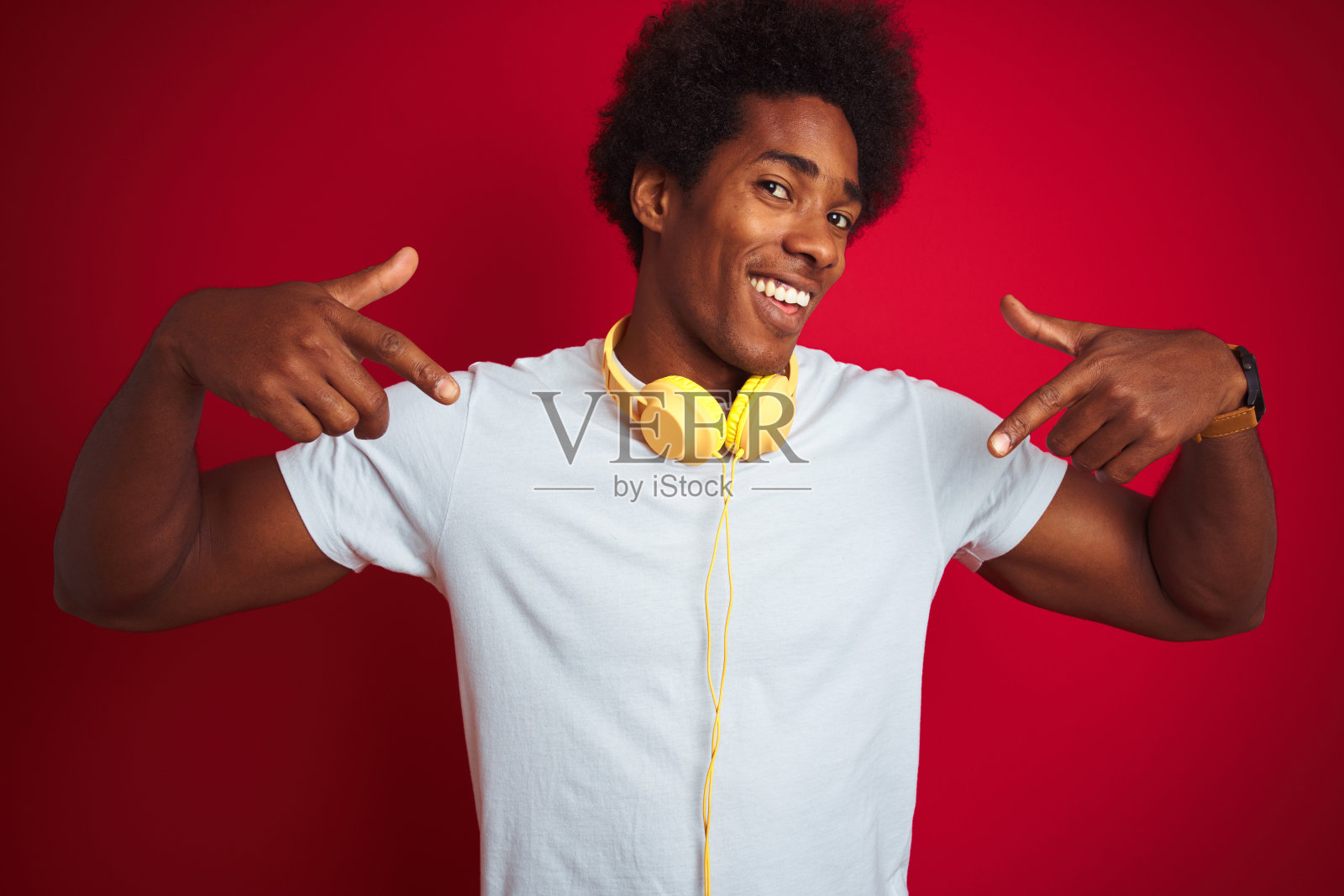 年轻的非洲裔美国人听音乐使用耳机在孤立的红色背景看起来自信的微笑，用手指指着自己骄傲和幸福。照片摄影图片