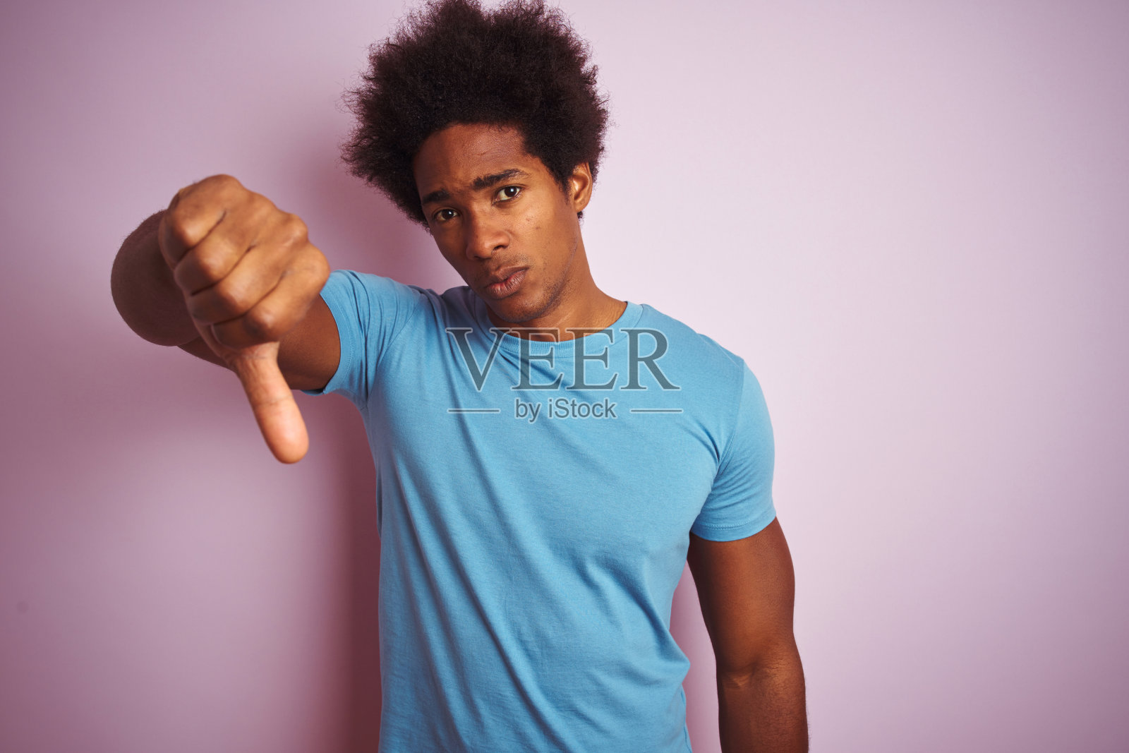 非洲裔美国人与非洲发式穿蓝色t恤站在孤立的粉红色背景看起来不高兴和愤怒显示拒绝和负面拇指向下的手势。糟糕的表达。照片摄影图片