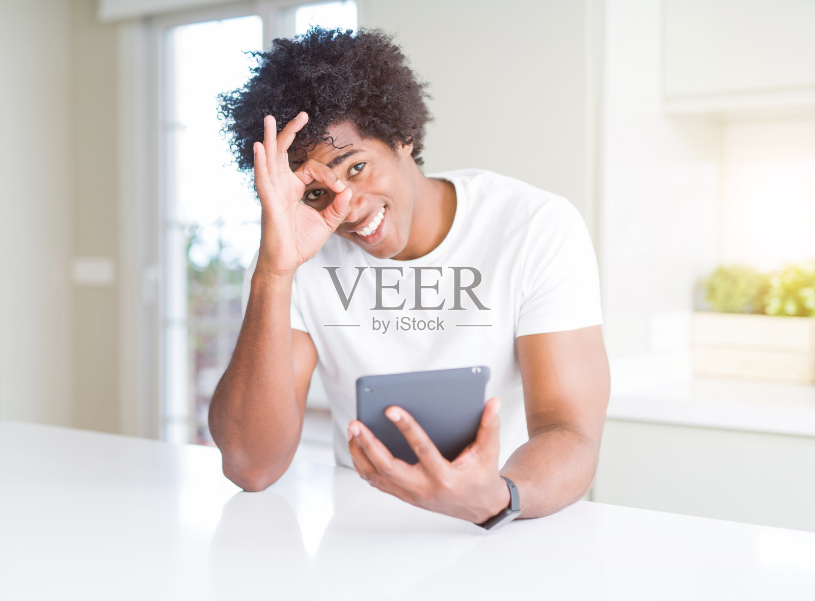 非裔美国人用触控板表与快乐的脸微笑做ok手势与手在眼睛透过手指看照片摄影图片