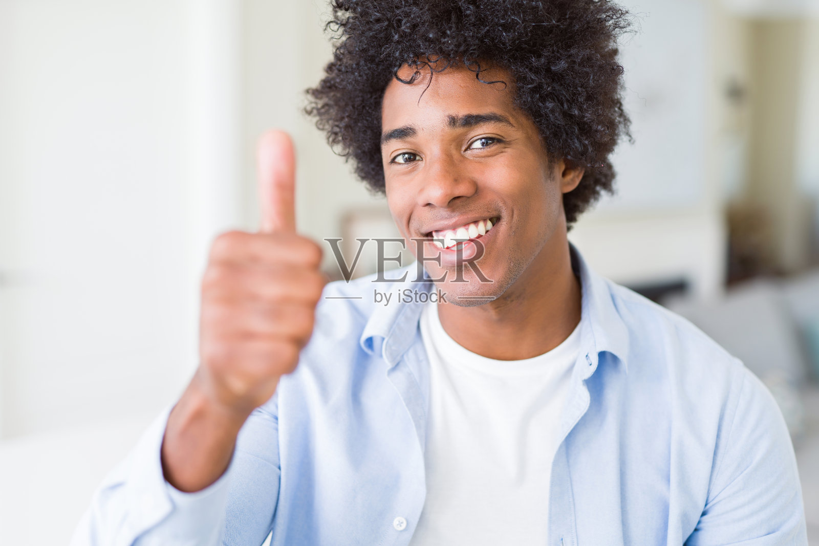 非裔美国人在家里做快乐的竖起大拇指的手势。赞许的表情看着镜头，表示成功。照片摄影图片