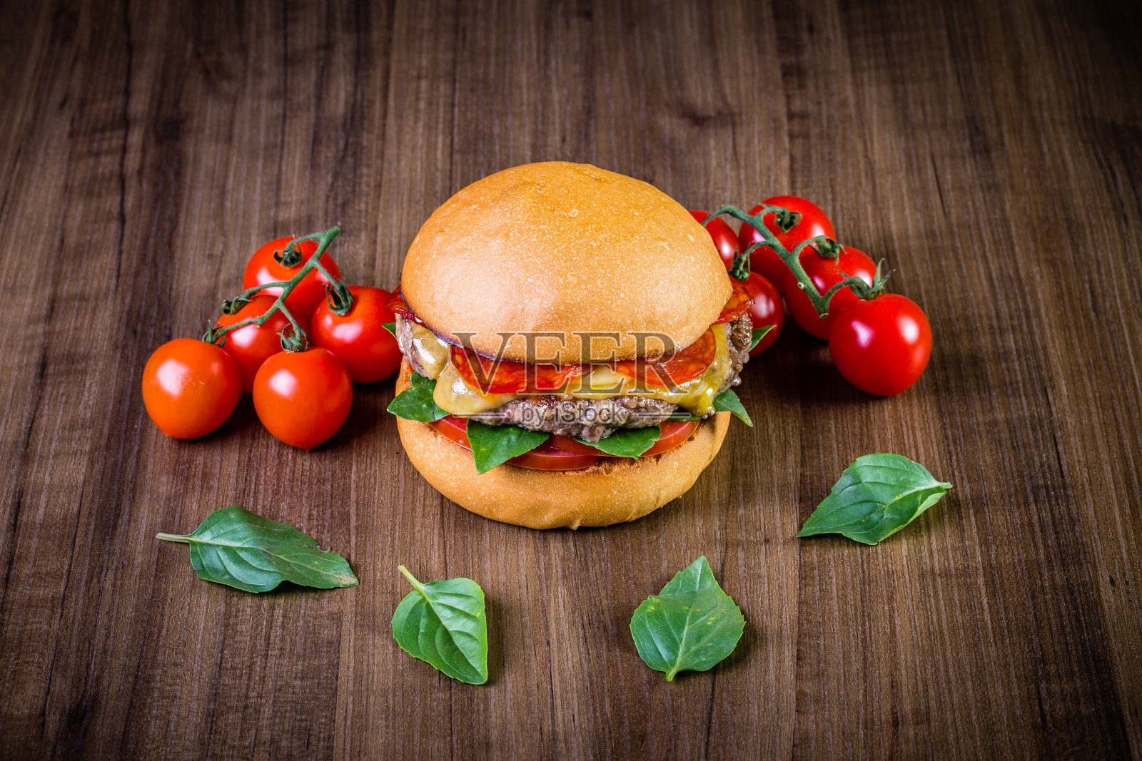 手工牛肉汉堡与奶酪，意大利辣香肠，番茄和罗勒叶木桌和乡村背景照片摄影图片