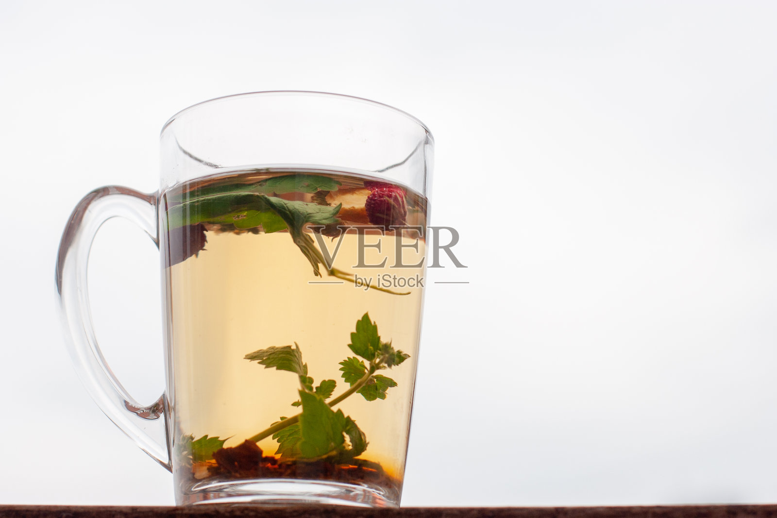 静物杯与花草茶。背景上是白色的天空。草莓叶和浆果漂浮在杯子里。照片摄影图片
