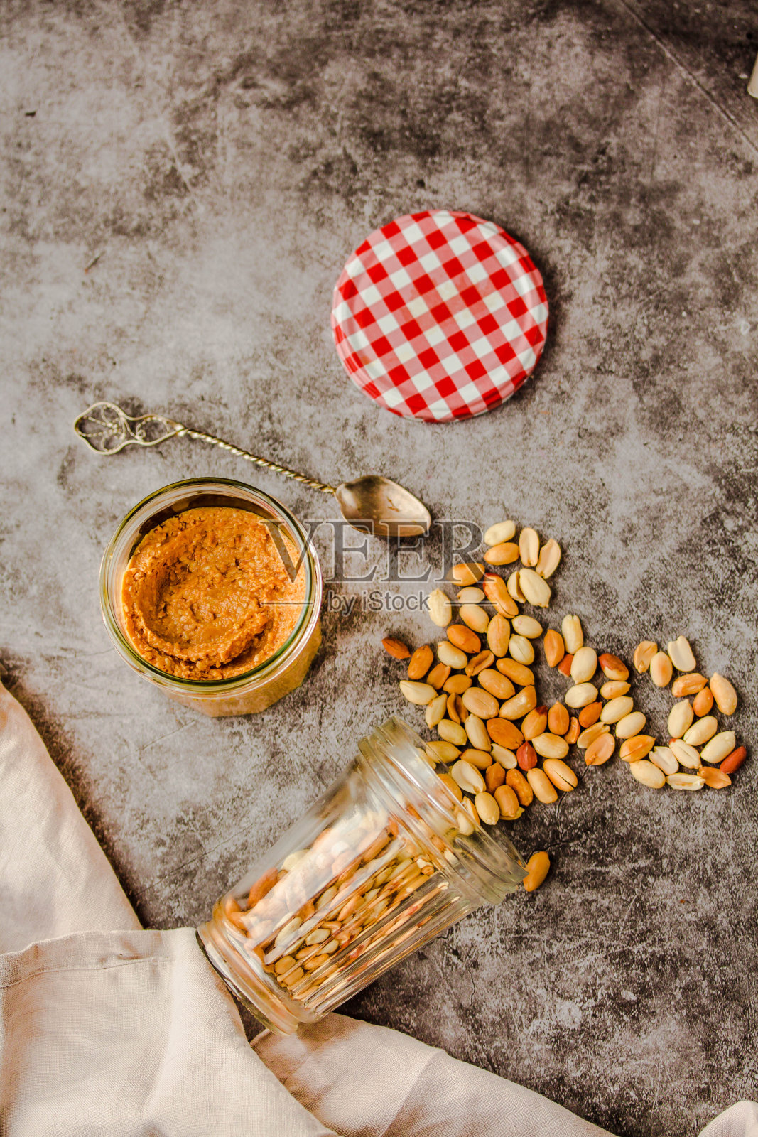 罐子和勺子的花生酱和花生在深色的木制背景从俯视图。亲属和舒适的食物氛围概念。照片摄影图片