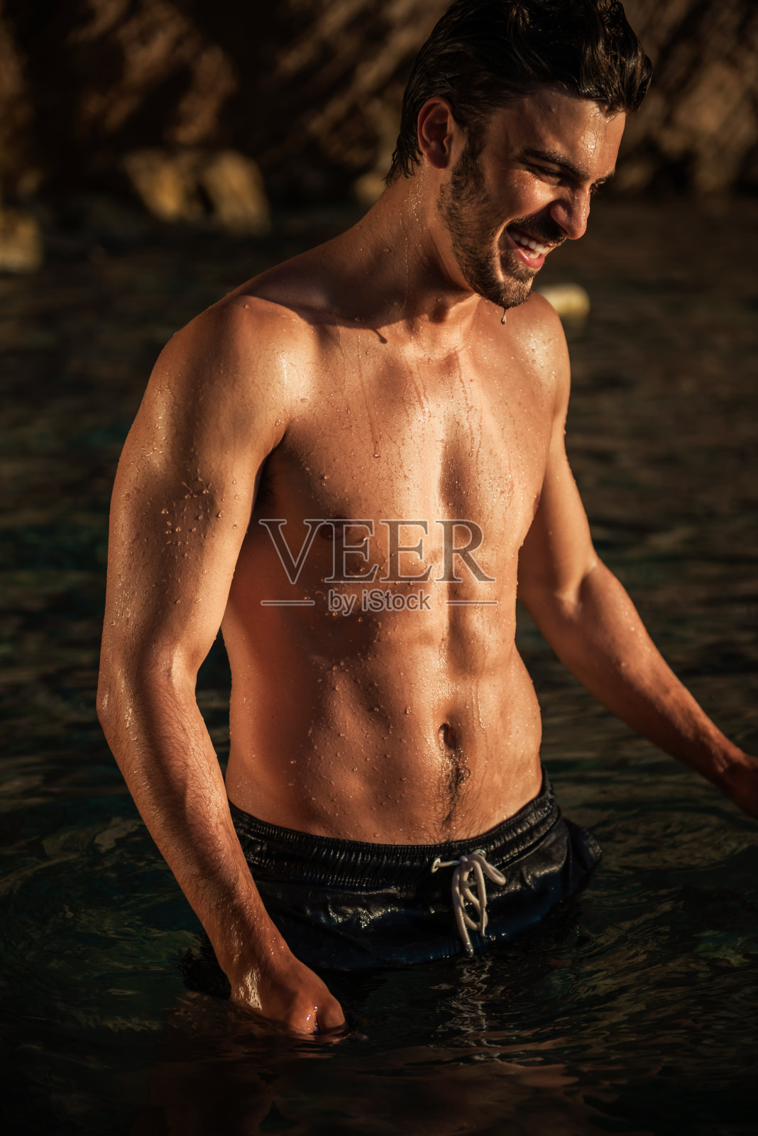 英俊的赤膊肌肉健美的人在海滩上，看一边和微笑照片摄影图片