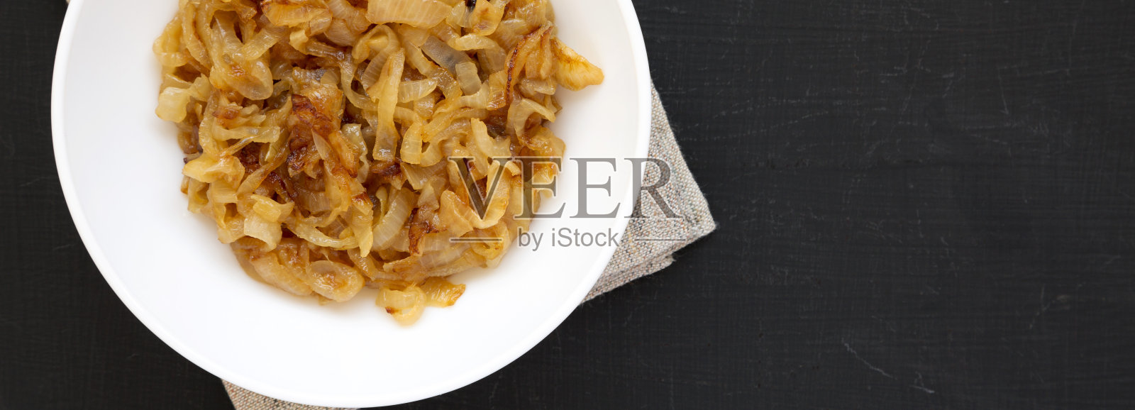 自制焦糖洋葱放在白色盘子上，黑色表面，俯视图。从上面，头顶上，平躺着。副本的空间。照片摄影图片