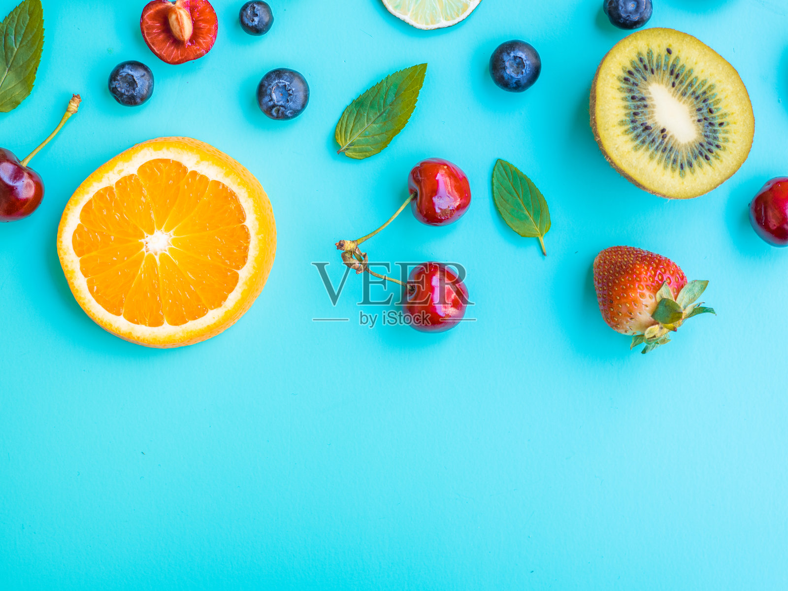 不同的水果，猕猴桃，樱桃，橙脂草莓，柠檬和罗勒绿叶孤立的蓝色照片摄影图片