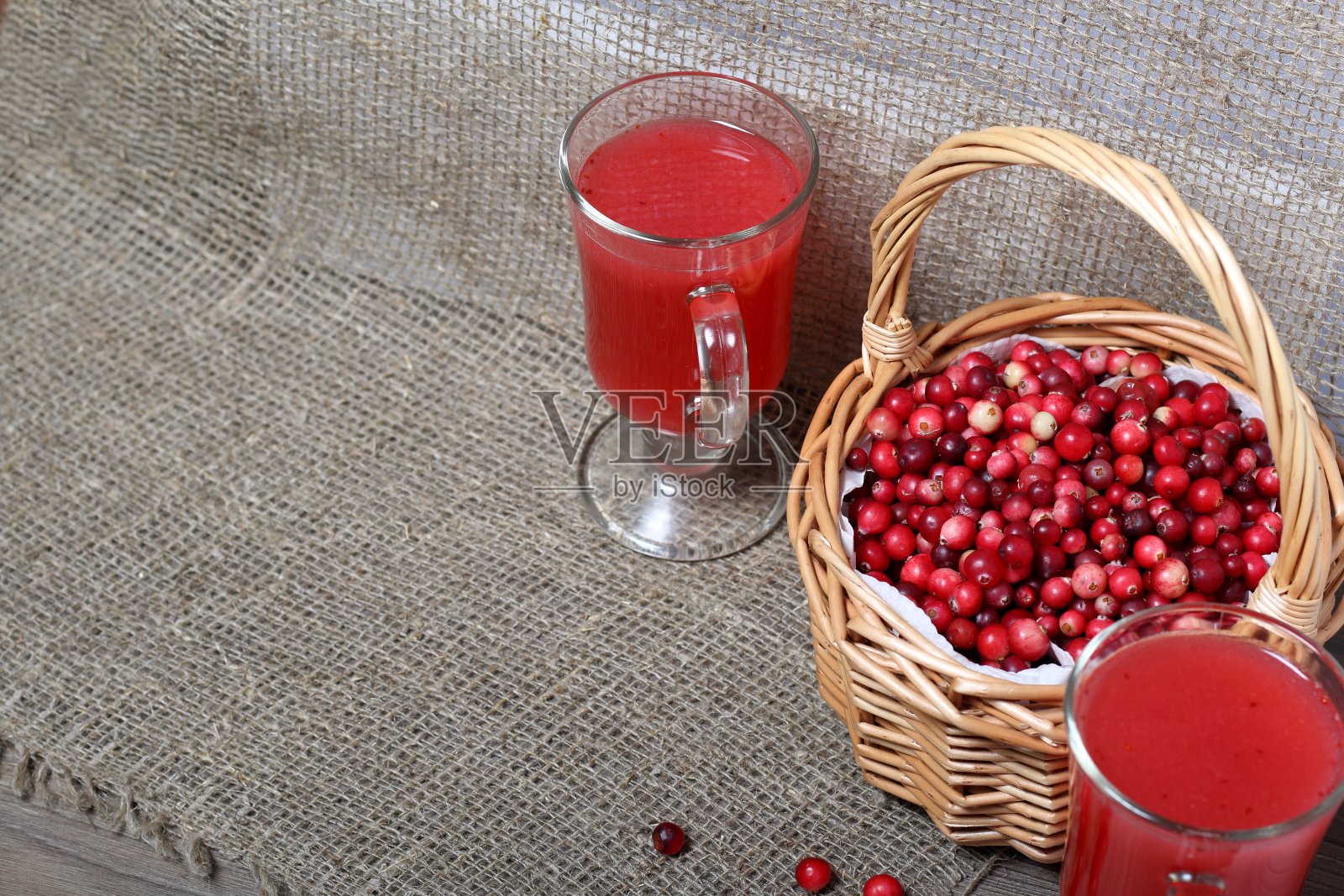 篮子里装满了蔓越莓。它矗立在一个覆盖着亚麻布的表面上。杯子旁边是蔓越莓汁。几颗浆果撒在表面上。照片摄影图片
