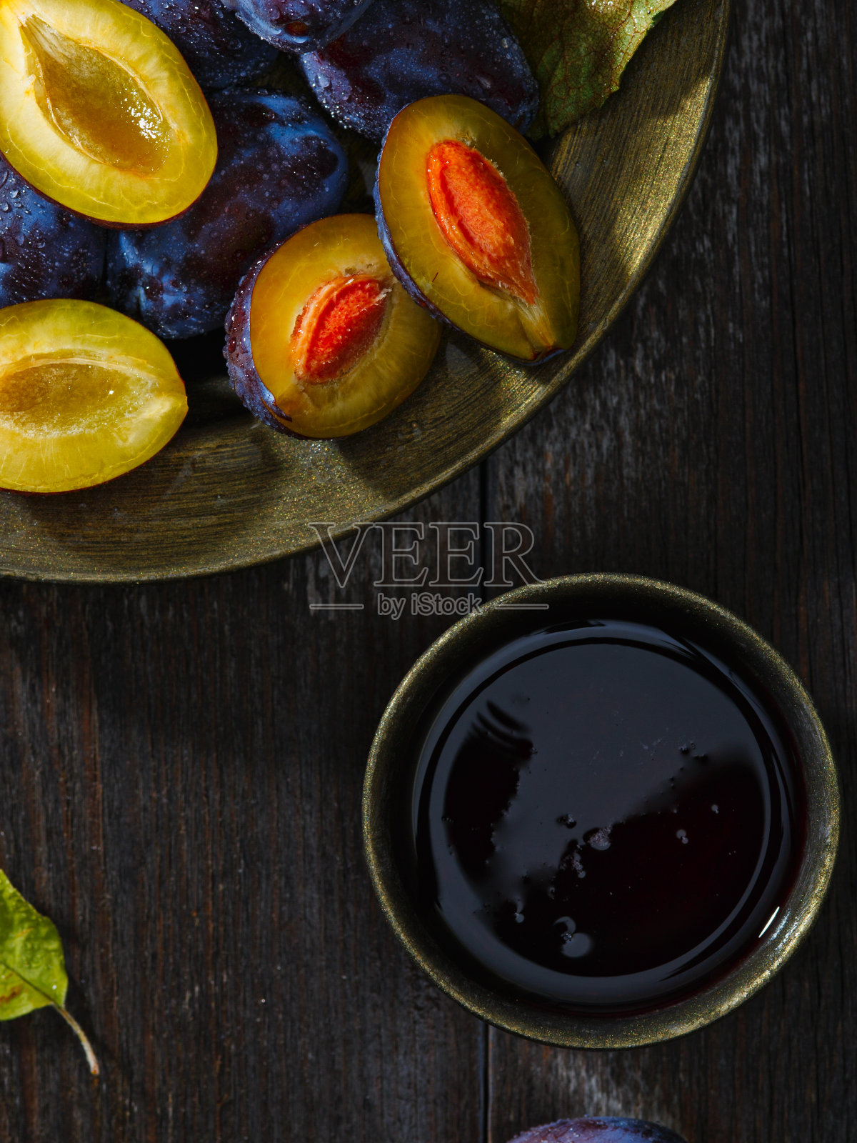 旧木桌上的陶瓷盘子里装着熟透的新鲜李子。黑暗的背景。前视图。照片摄影图片