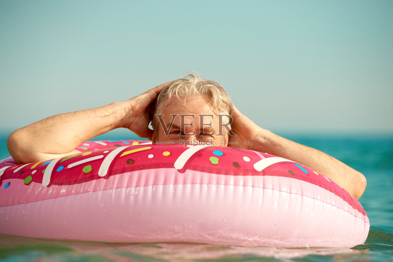 一个头发灰白的滑稽男子在海里绕着一个充气圈游泳照片摄影图片