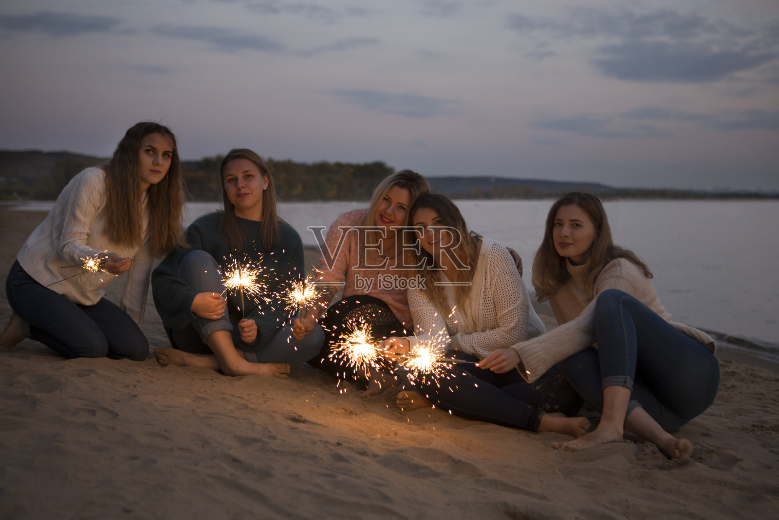 一群快乐的朋友在海滩上享受烟花派对。照片摄影图片