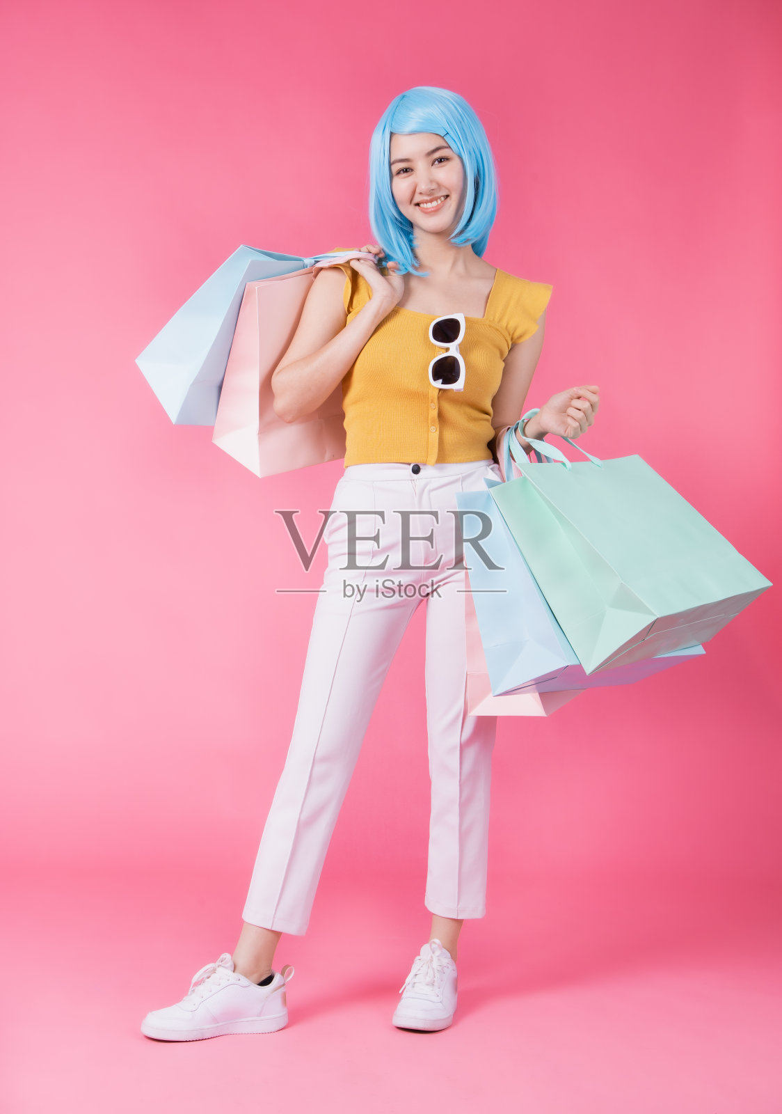 一个漂亮兴奋的亚洲女孩的肖像与彩色购物袋显示孤立在粉红色的背景。亚洲购物狂妇女携带彩色的夏季销售概念购物袋。年轻的蓝色头发女孩。照片摄影图片