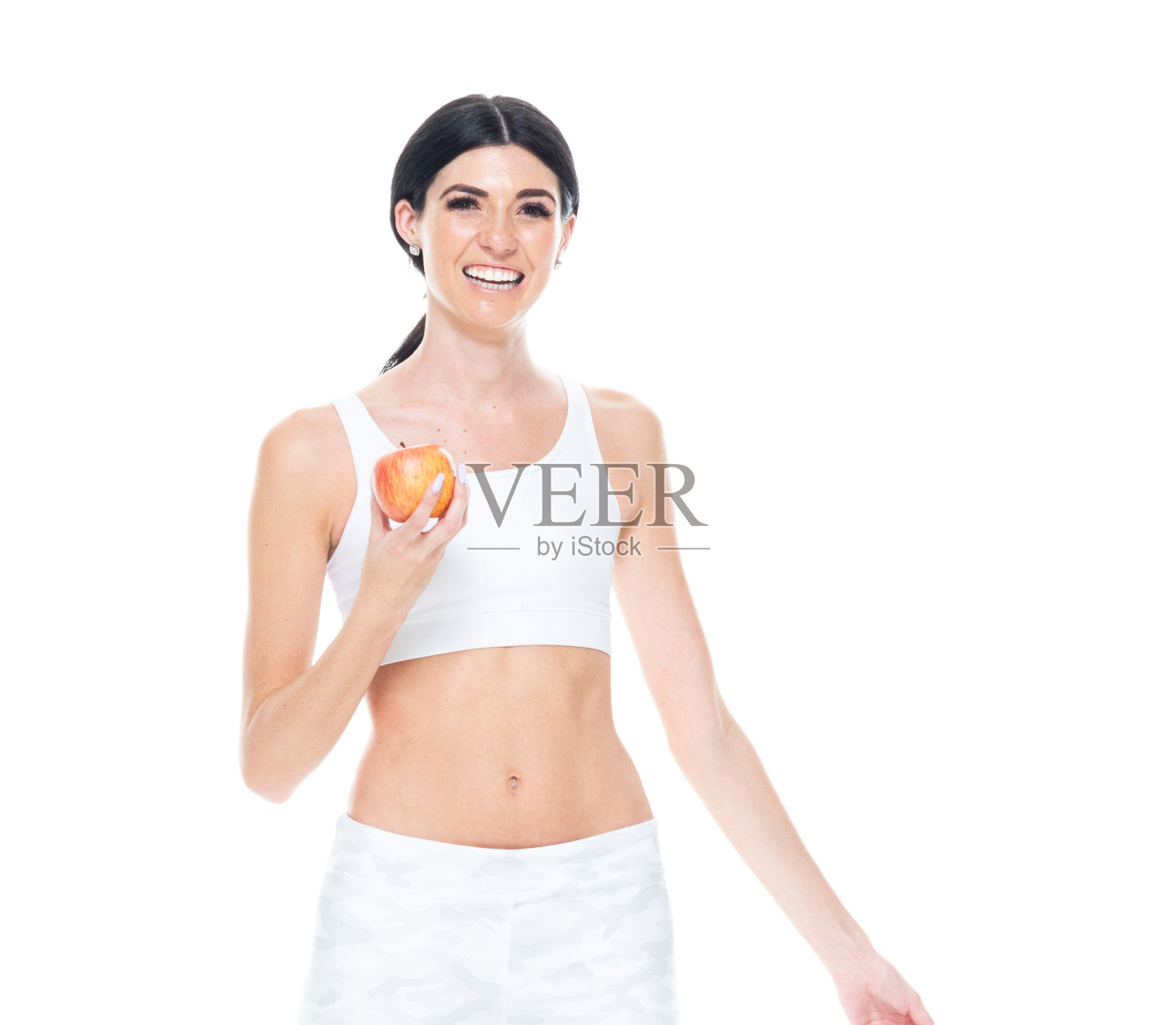 一个人/正面视图/腰部以上的20-29岁的成年人美丽/高个子/长发白种人年轻女性/女性在白色背景穿着弹性纤维/运动胸罩/打底裤谁是微笑/快乐/愉快的拿着水果照片摄影图片