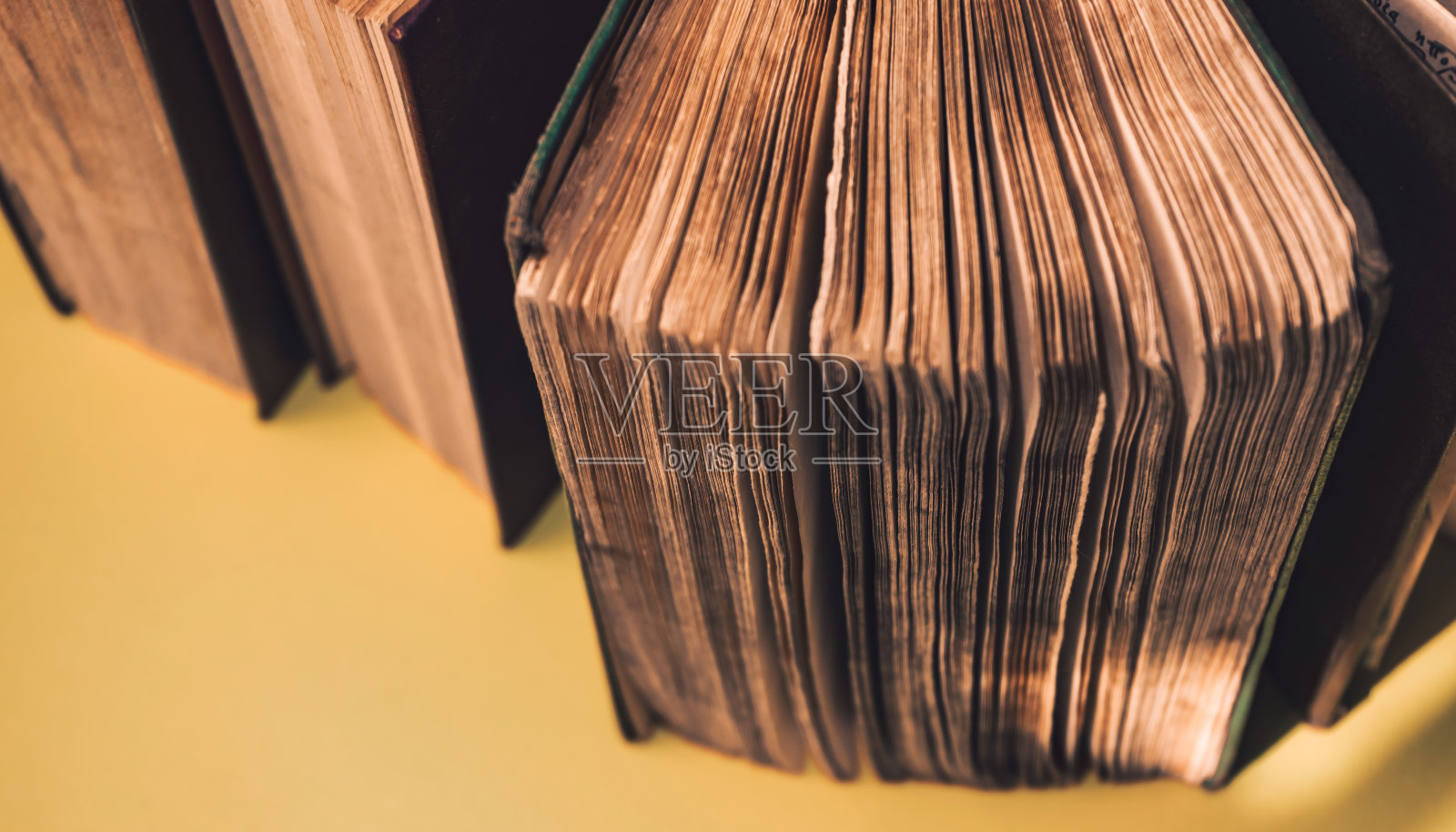 把黄色背景桌子上打开的旧书合起来。宏观的观点。照片摄影图片