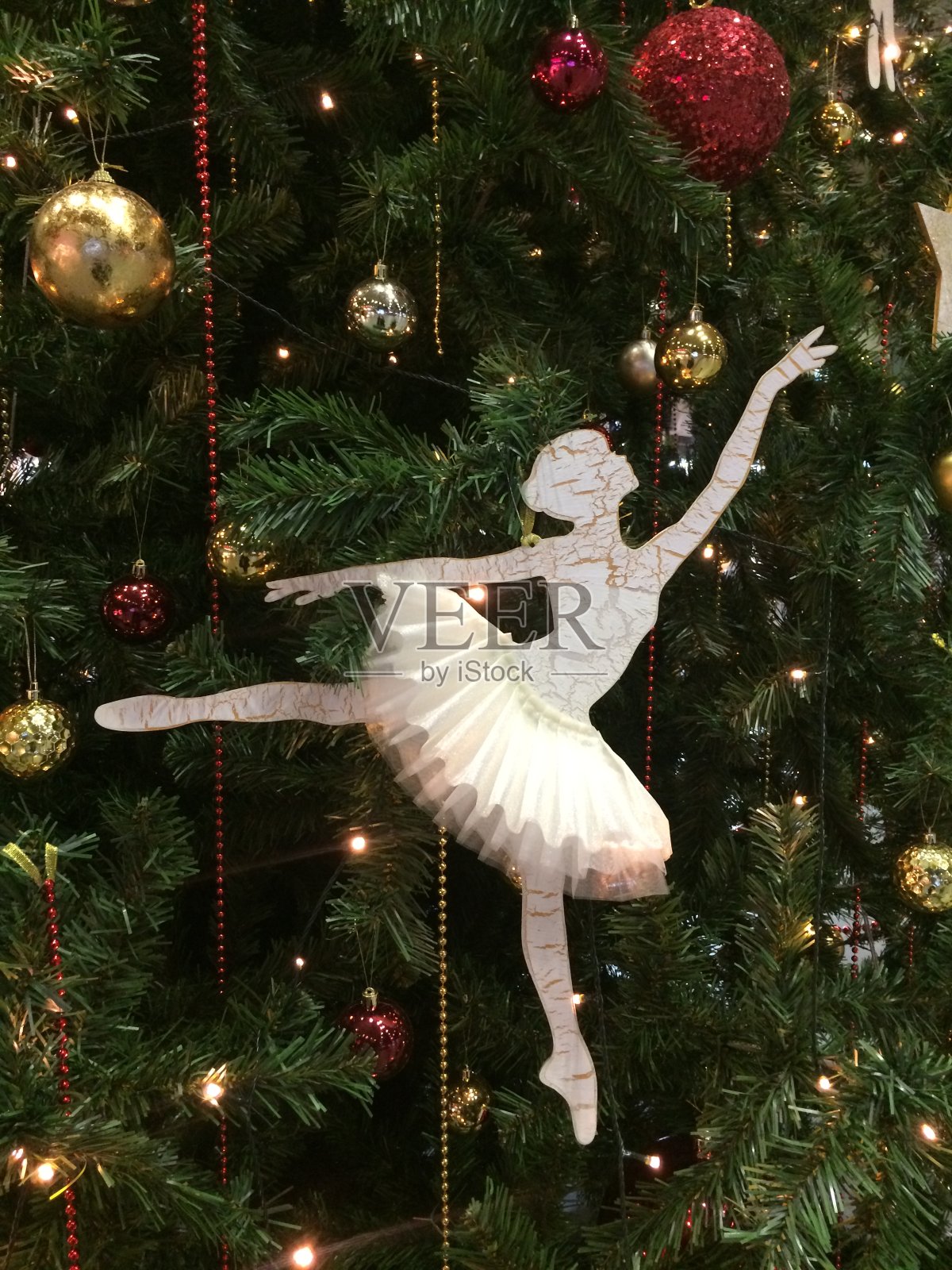 美丽的纸芭蕾舞演员装饰圣诞树的树枝。节日背景是一棵绿色的圣诞树和金色和红色的小球和珠子。照片摄影图片