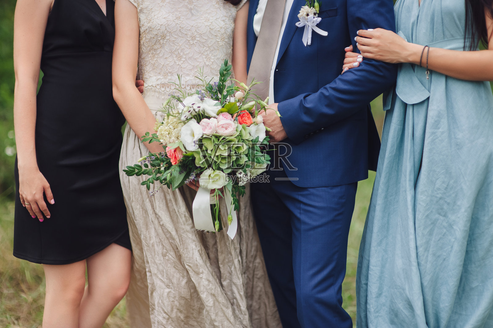 新婚夫妇站在大自然中，与朋友拥抱，手持一束野花。婚礼上的伴娘。婚礼的细节。照片摄影图片