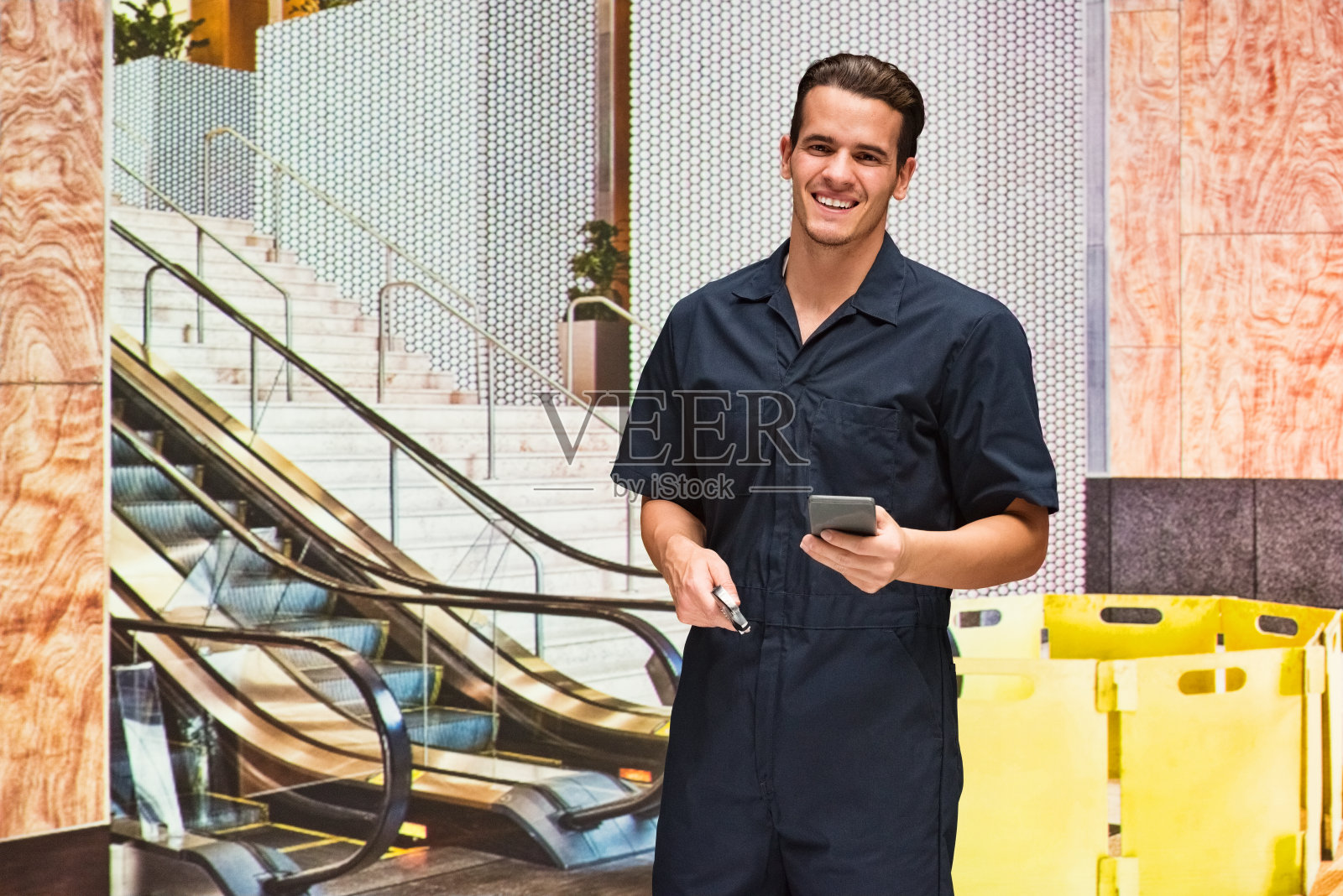 一人/一人/腰部以上/ 20-29岁的成年人英俊的人白人男性/年轻男子修理工/技术员/手工工人/服务职业修理在自动扶梯前穿着工作服的人正在工作/大厅照片摄影图片
